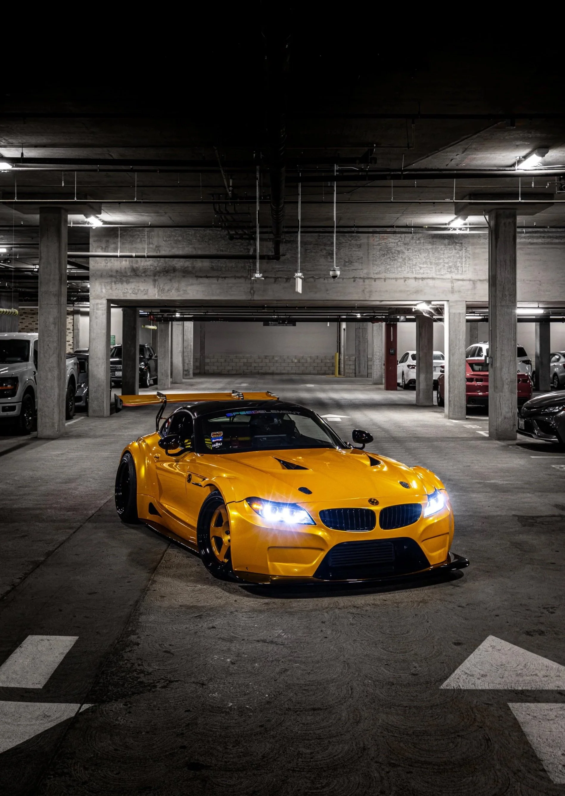 A yellow race car with a black spoiler parked in an underground parking garage.