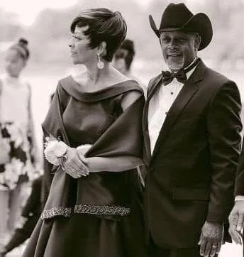 A woman in an elegant gown and a man in a tuxedo with a cowboy hat walking together at an outdoor event.