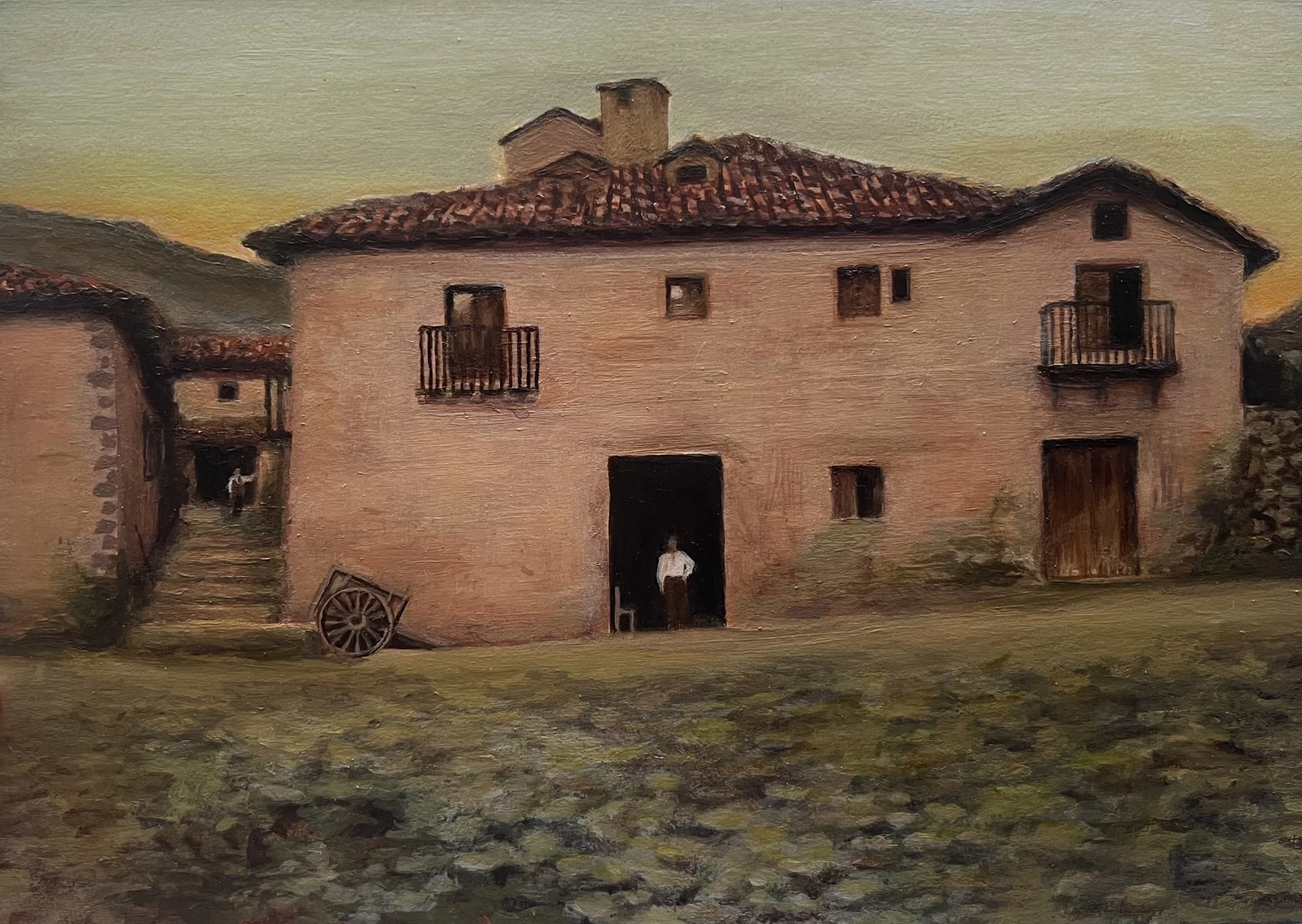 A rustic rural scene depicting a large stucco house with a red tile roof, small windows, and balconies at sunset, with an old wooden cart leaning against the wall and a person standing in the doorway.
