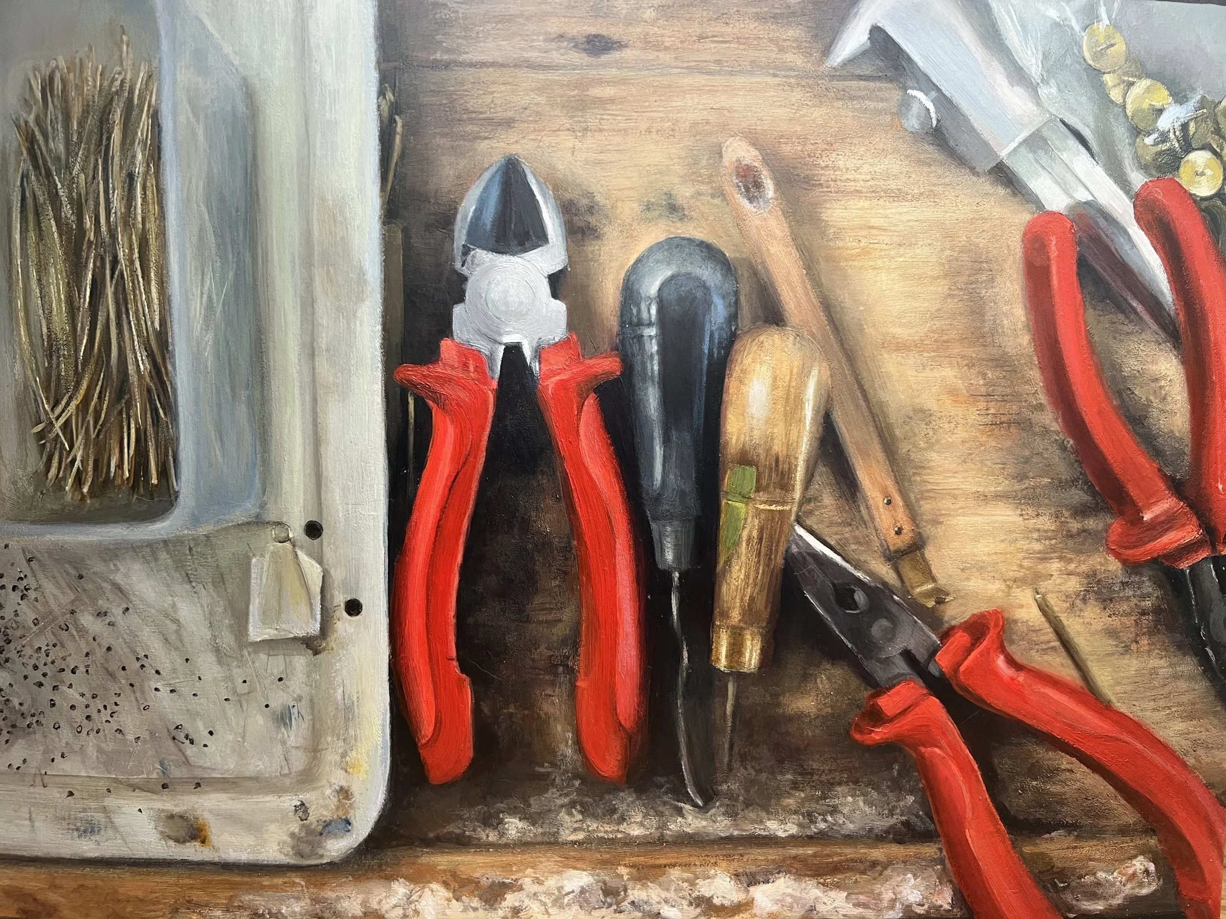 A collection of tools on a workbench including pliers, a knife, a saw, and a wrench, next to a container with a bundle of nails.