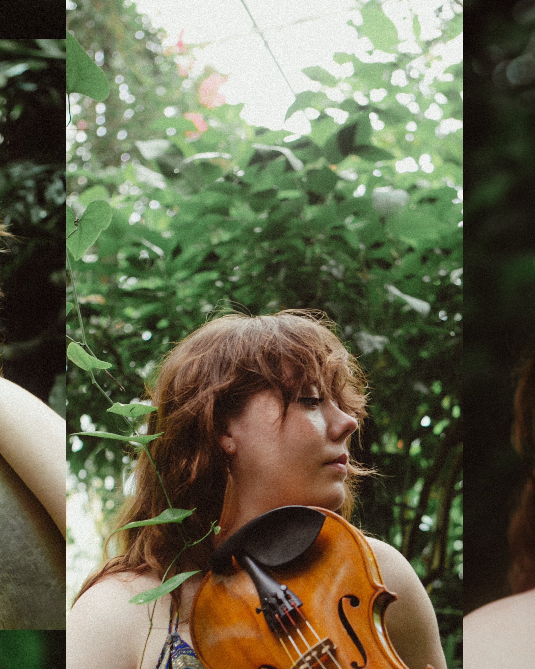 A photo of Meg with wavy brown hair holding a violin among green foliage.