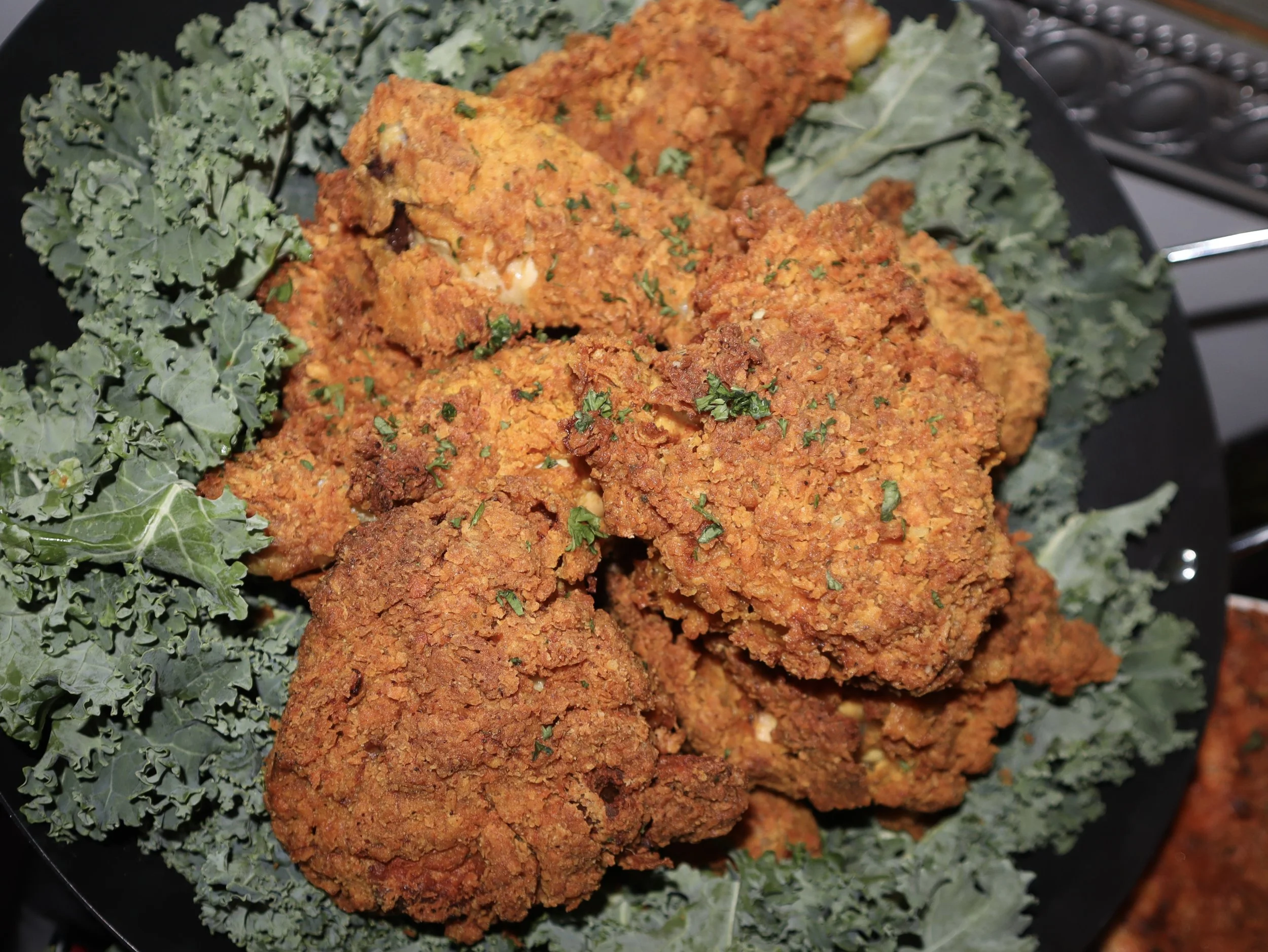Plate of fried chicken pieces garnished with parsley, served on bed of kale leaves.