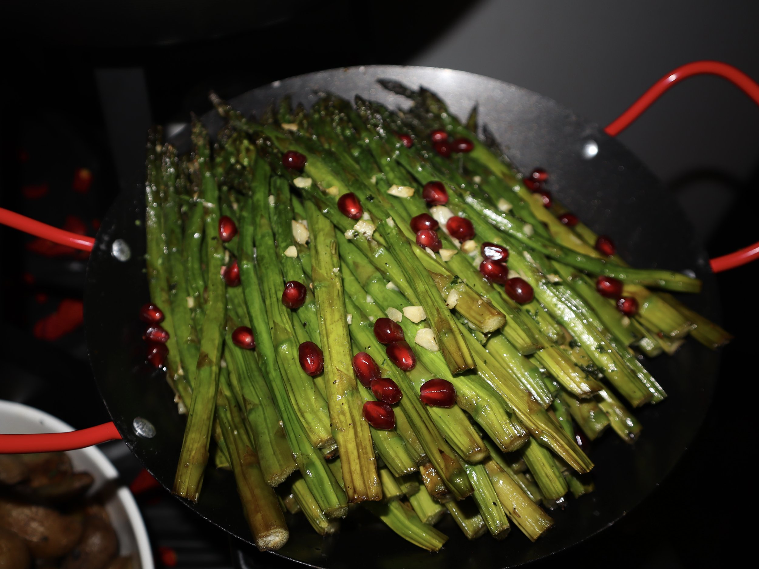 Cooking green onions with red pomegranate seeds and chopped garlic in a black skillet.
