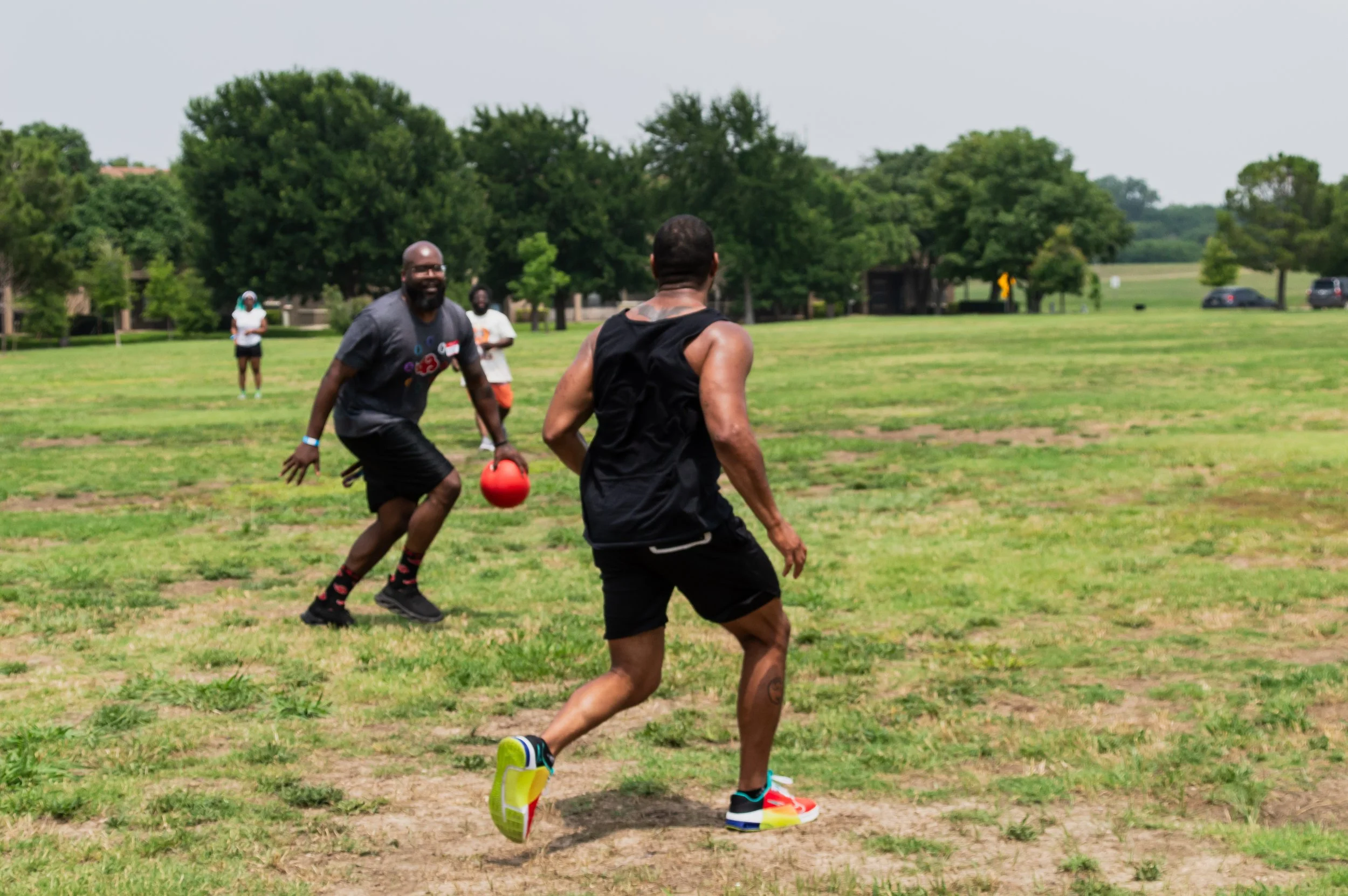 People playing flag football on a grassy field with trees in the background, one person holding a red flag, others running.