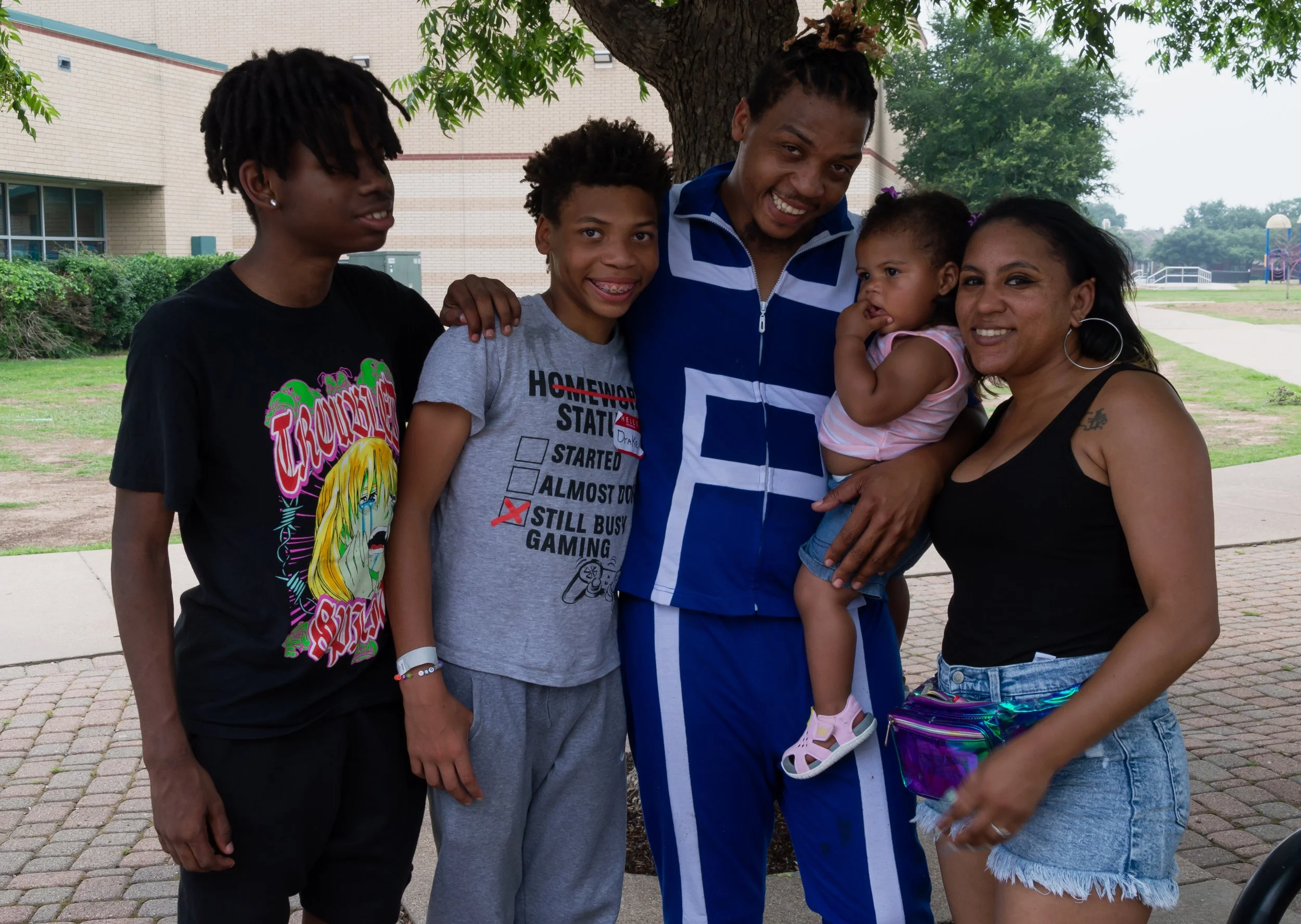 A family of six outdoors under a tree, smiling, with two young children and four adults.