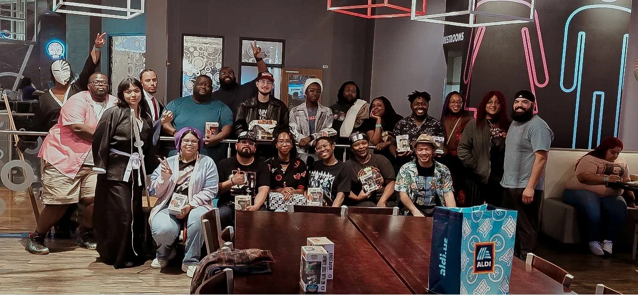 Group of diverse people gathered in a room with neon lights, some holding board game boxes, and a large ALDI shopping bag on the table in front.