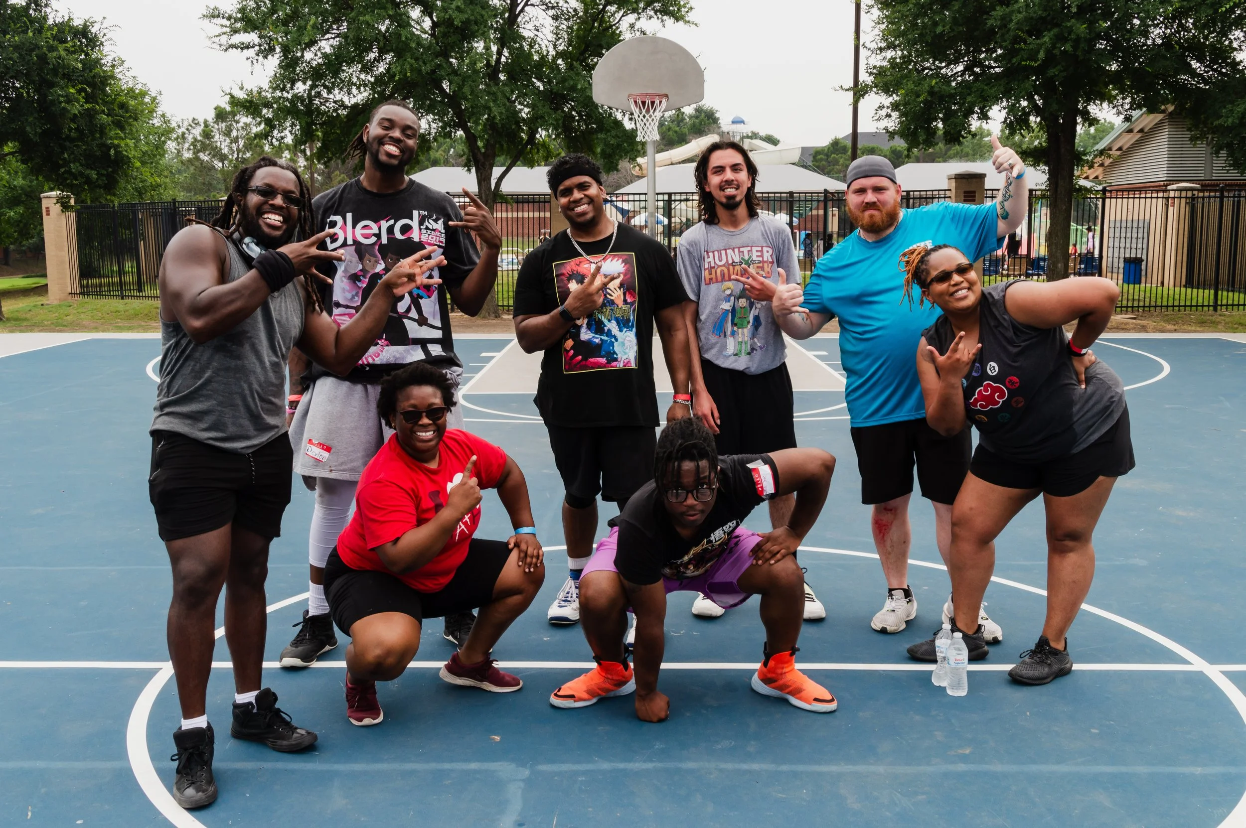 Group of nine people posing and smiling on a basketball court outdoors.