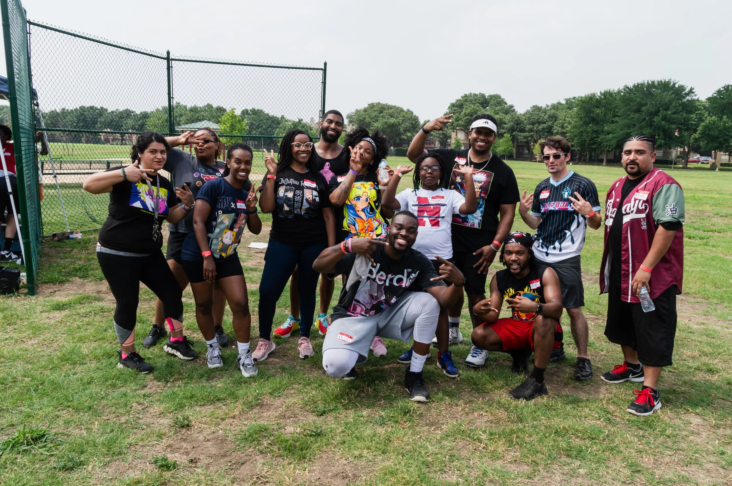 A diverse group of people posing outdoors on a grassy field, making peace signs and smiling.