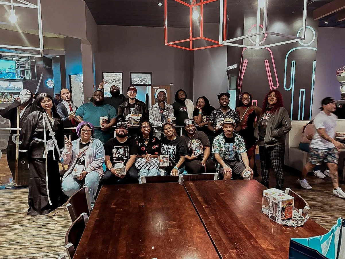Group of people posing for a photo inside a modern restaurant or cafe, with some people holding boxes, and neon pink and blue light designs on the wall in the background.
