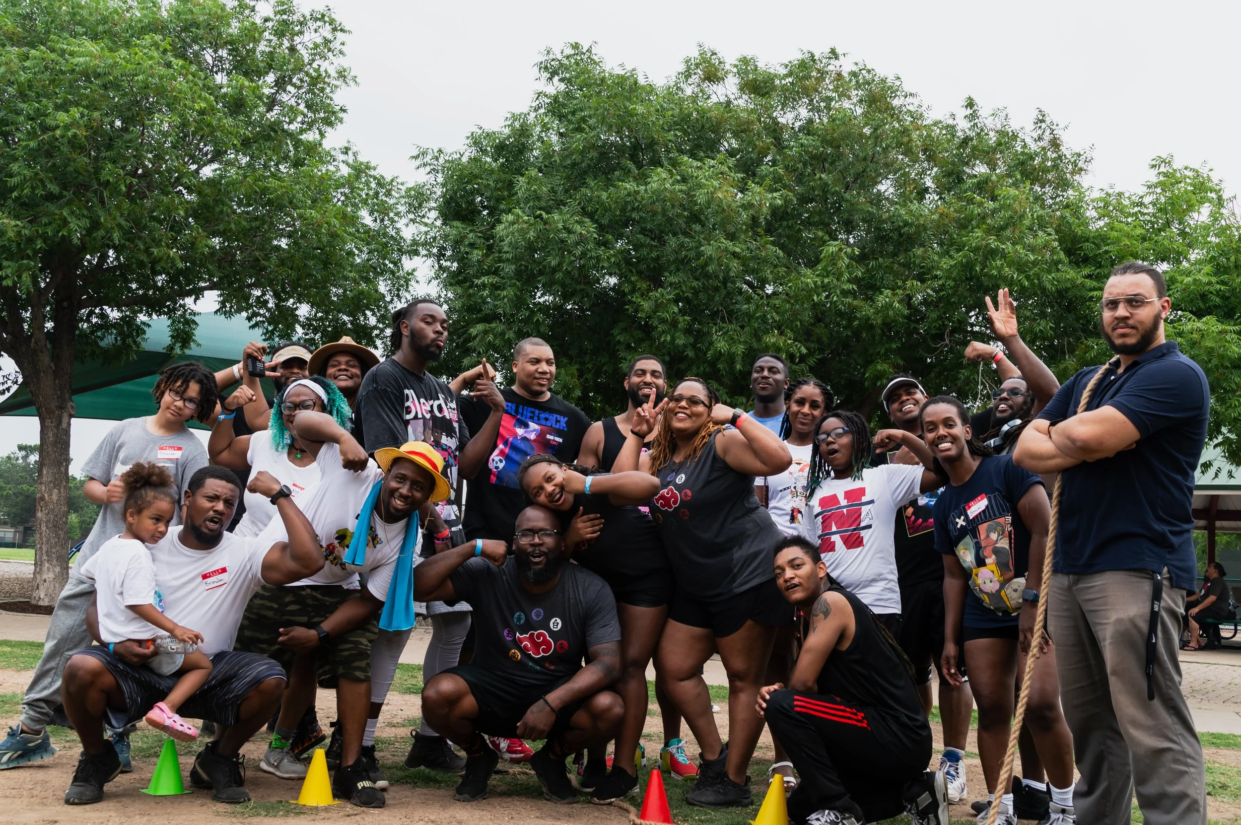 Group of people outdoors posing for a photo, some flexing muscles, with trees in the background and colorful cones on the ground.