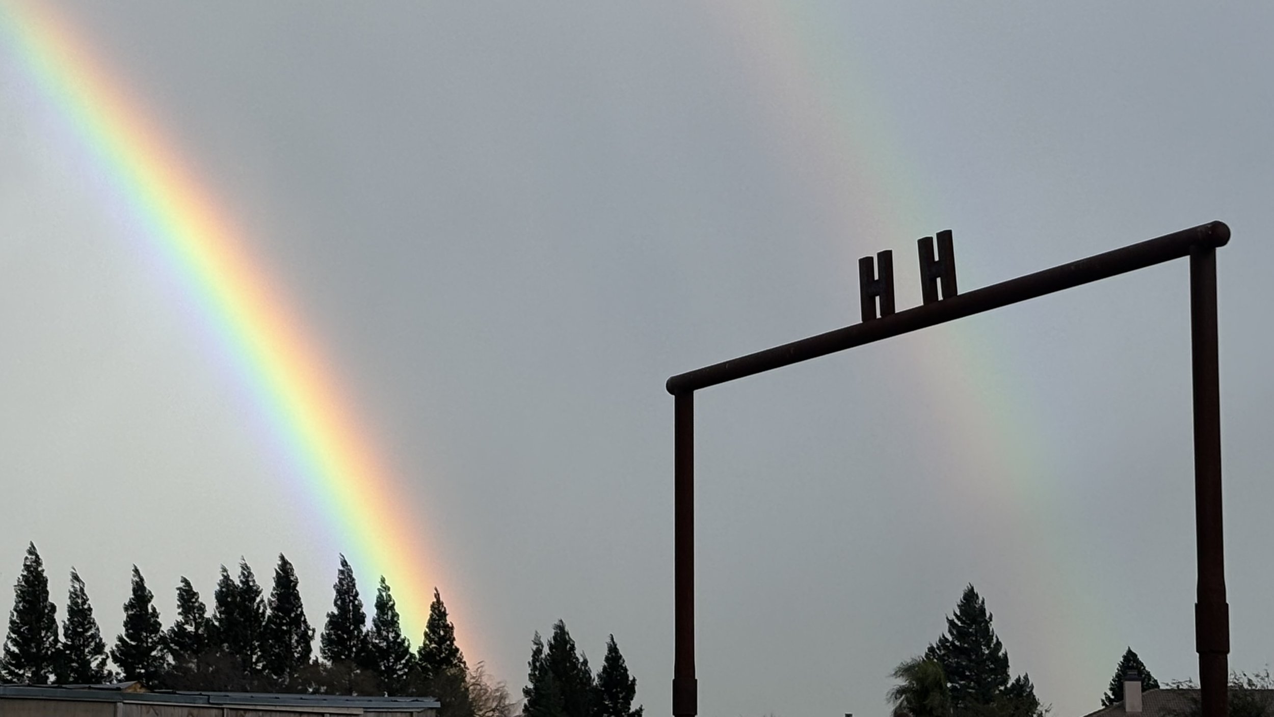 Double rainbow in the sky above trees, with a sports goal post in the foreground.