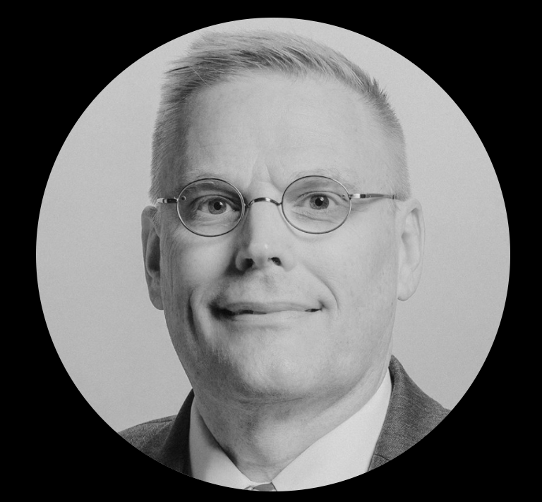 Black and white headshot of a man wearing glasses and a suit, smiling slightly.