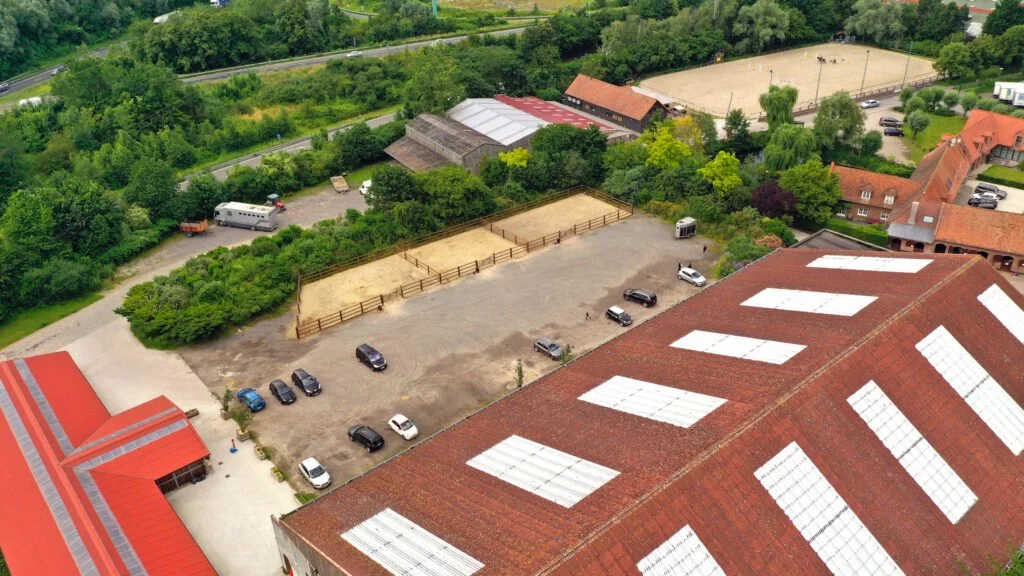 vue aérienne d'un parking avec voitures, abris de toit rouge, terrains de sport et bâtiments entourés de végétation