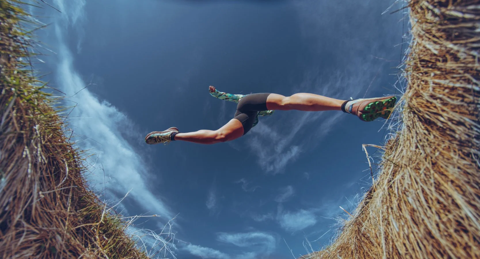 Athlete running on a straw field with blue sky and clouds above.