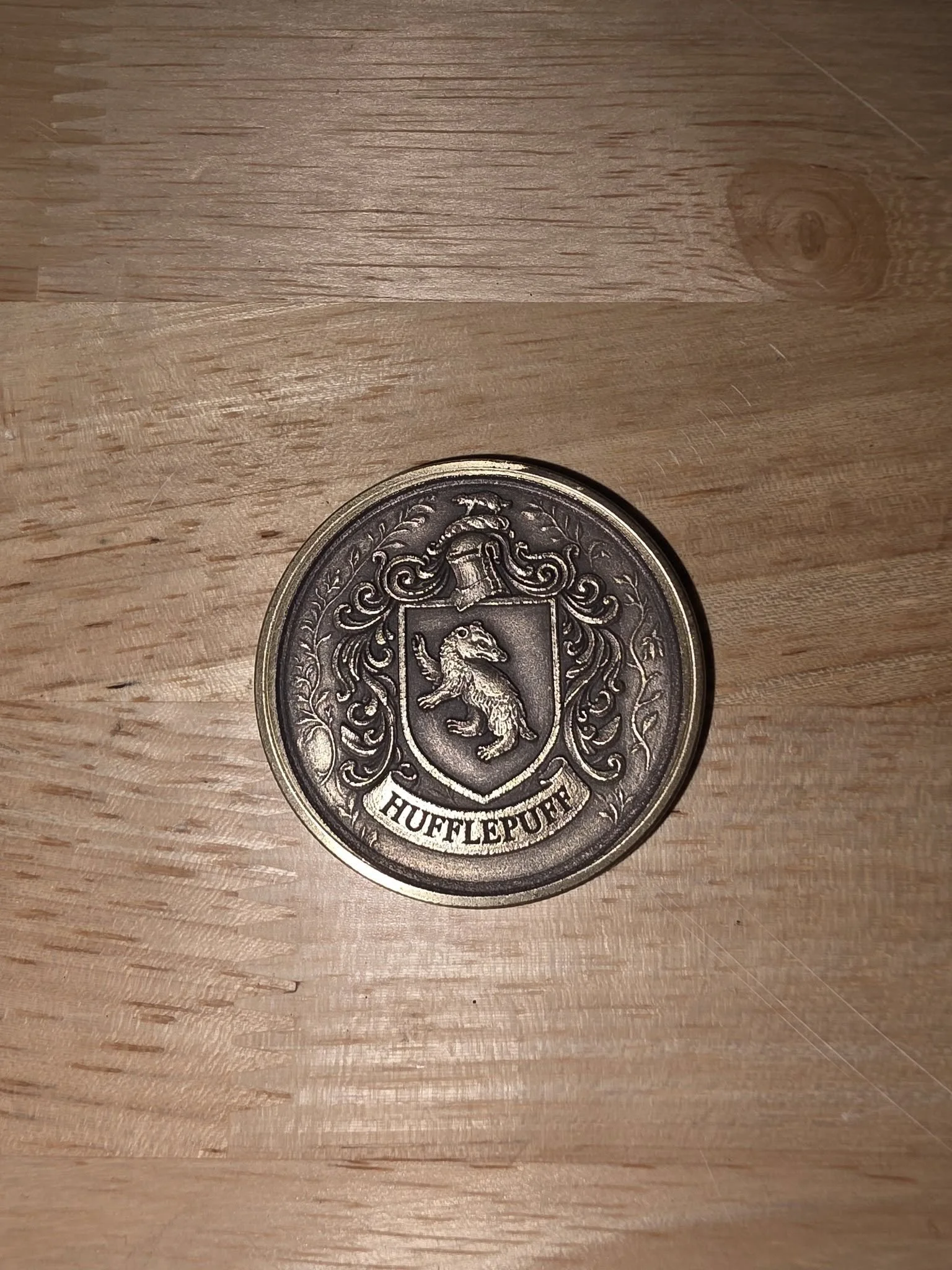 A round coin with a lion on a shield and the word 'HUFFLEPUFF' at the bottom.