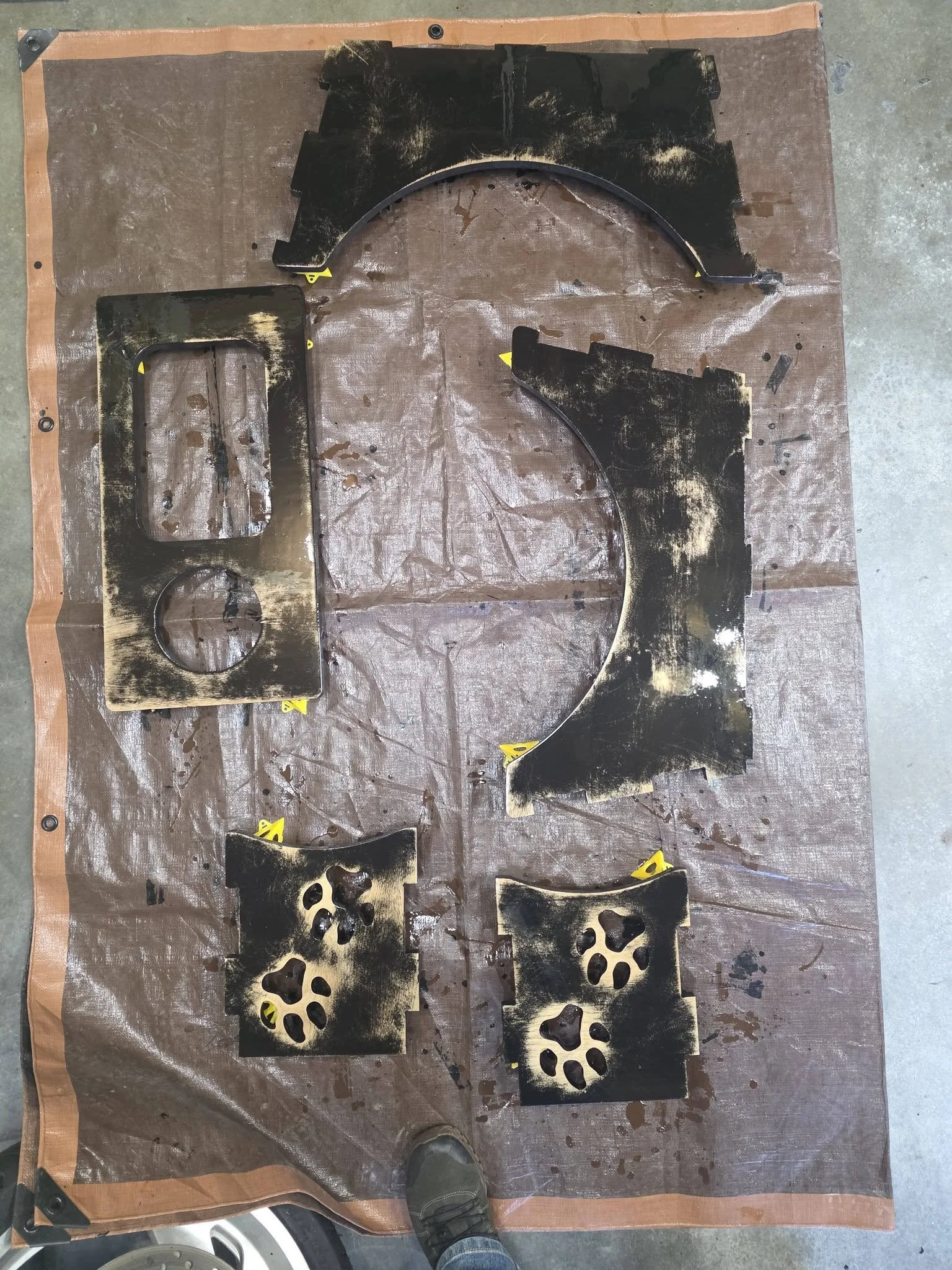 Various black painted and partially burnt metal pieces laid out on a brown protective sheet, possibly for painting or restoration work.