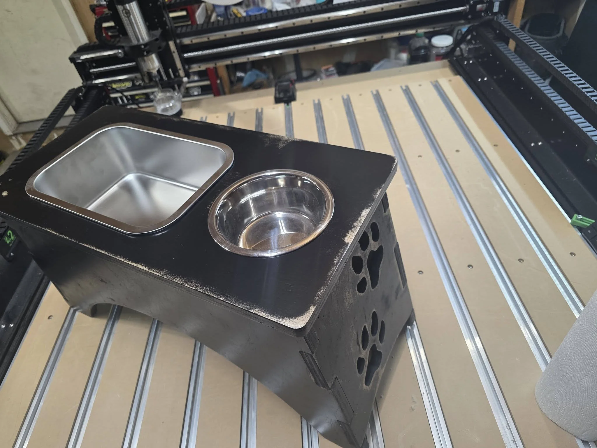 A black box with two metal bowls, one square and one round, is placed on a metal table in a workshop.