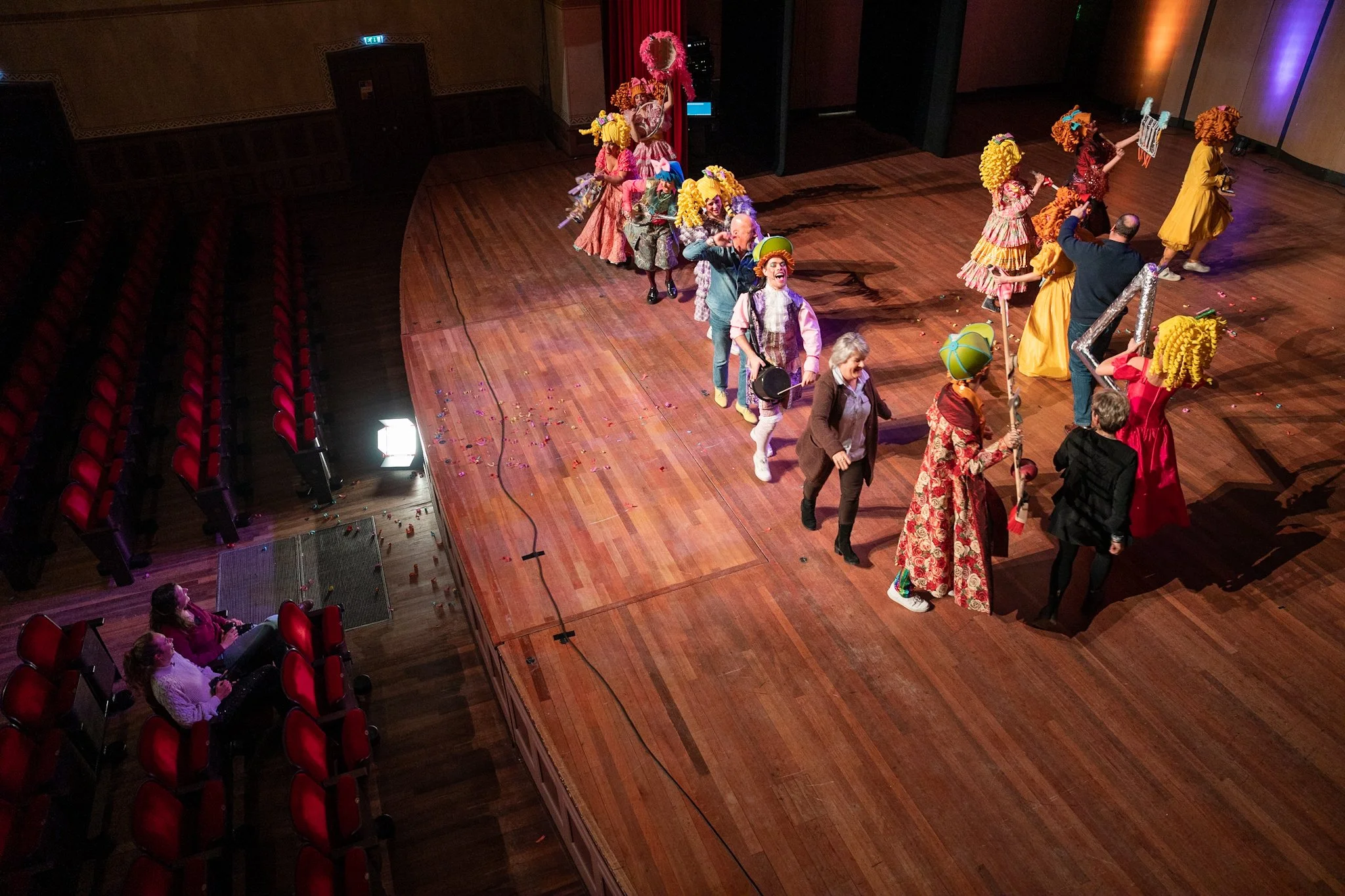Theatergroep op een podium met kleurrijke kostuums en maskers.