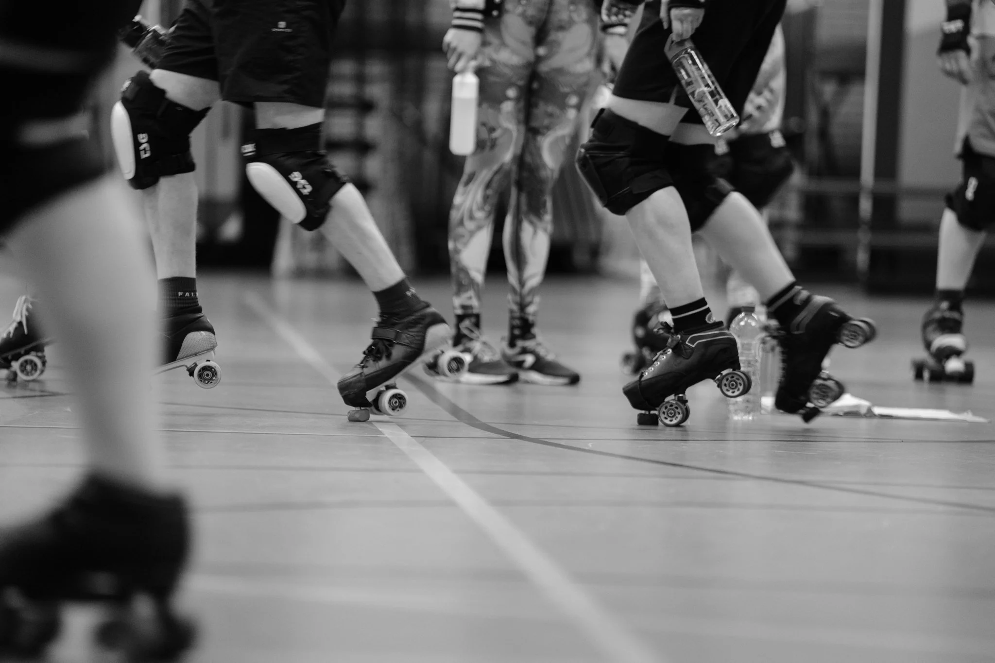 Mensen die inline skaten in een sporthal, deels te zien van de knieën en onderbenen, zwart-wit foto.