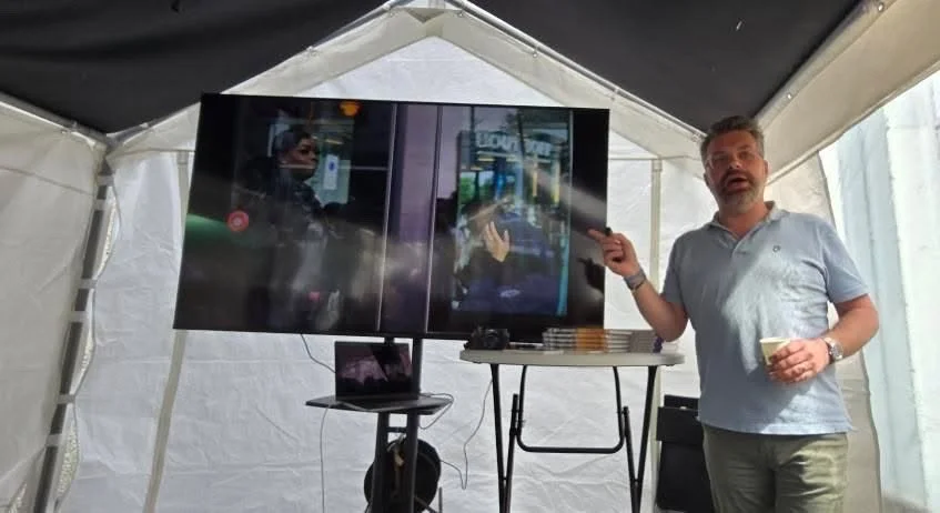 Man geeft presentatie voor een grote tv-scherm in een tent.