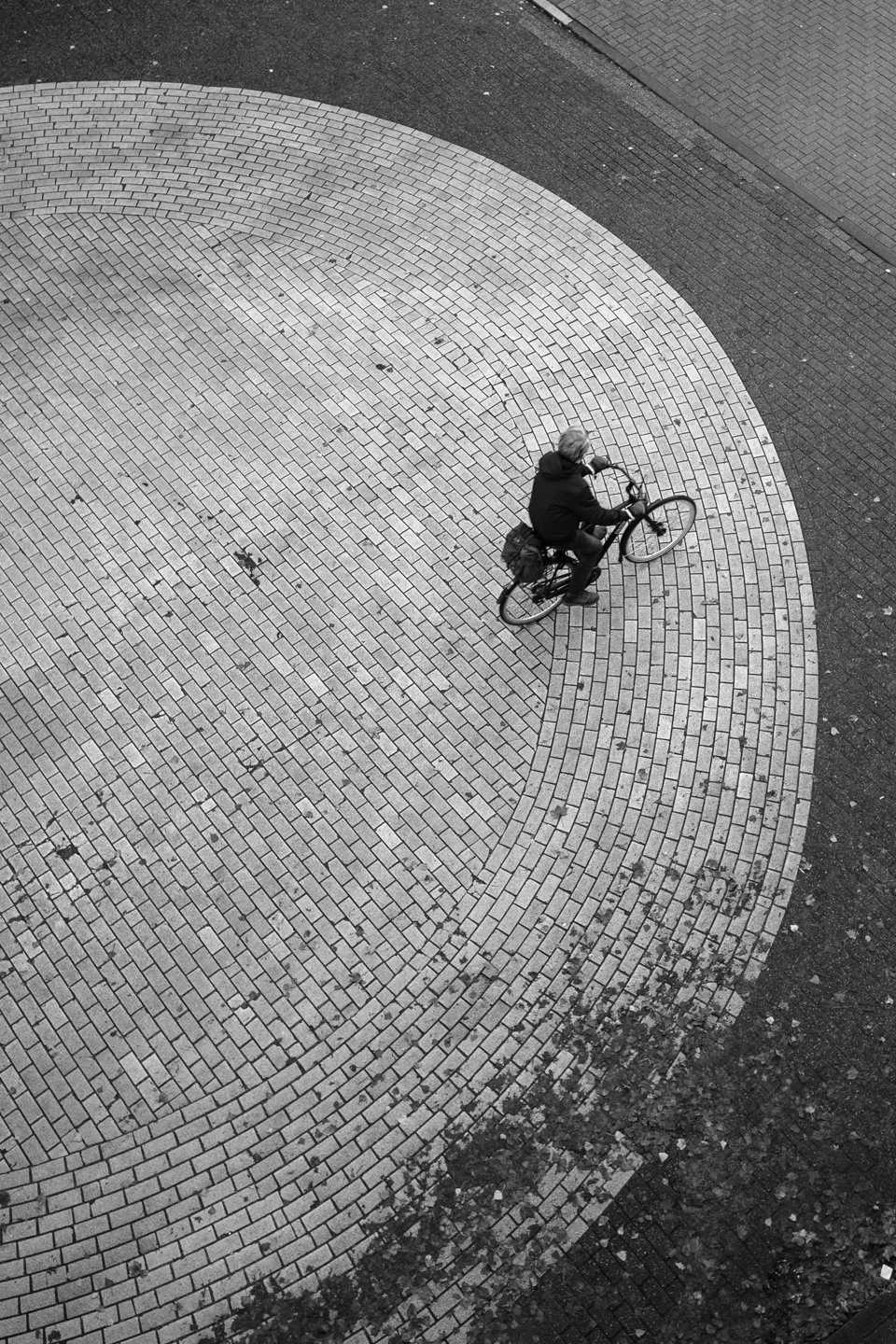 Een vogelperspectief van een persoon die op een fiets rijdt op een stenen gebogen straat of plein.