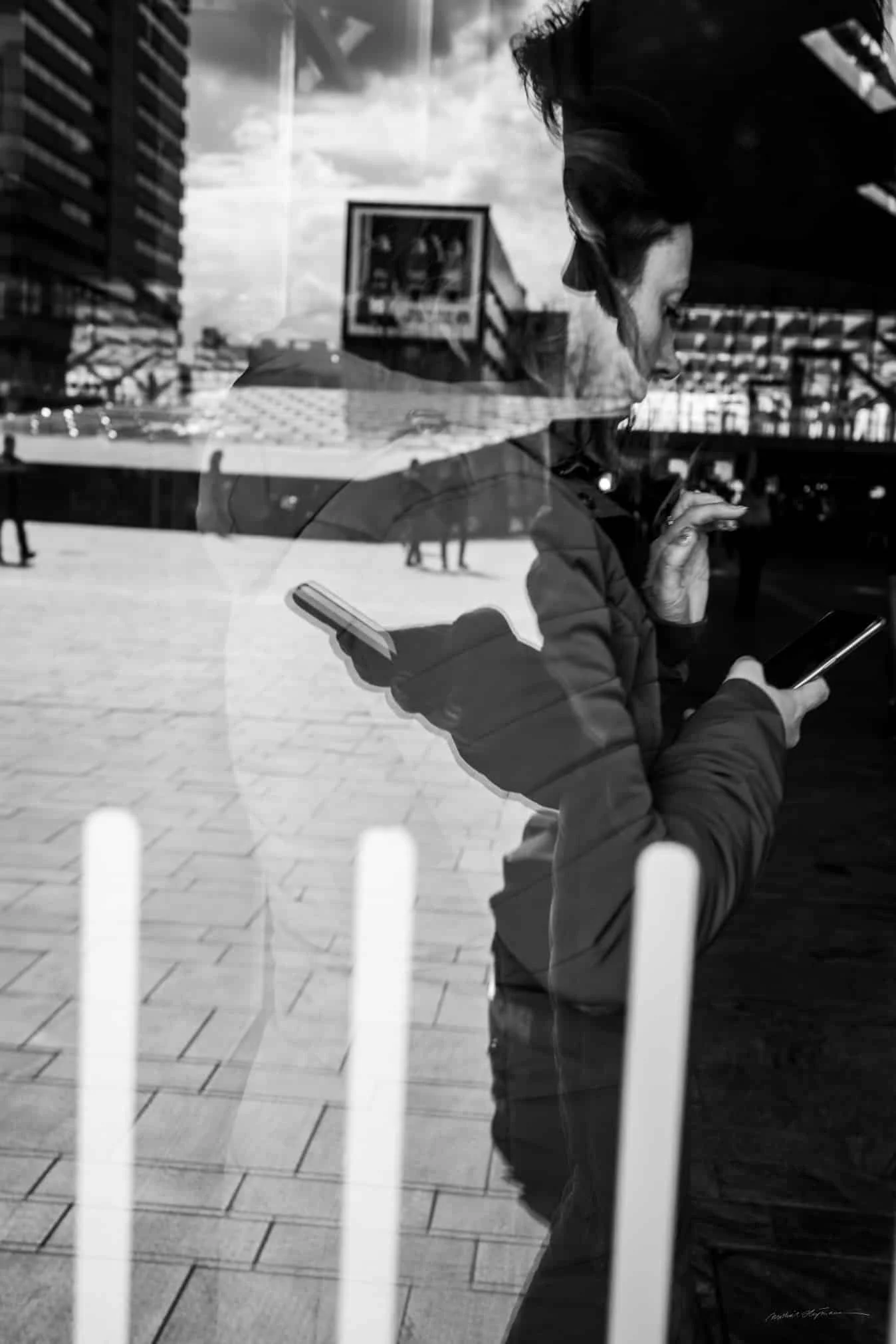 Een vrouw die achter een raam staat en op haar mobiele telefoon kijkt.