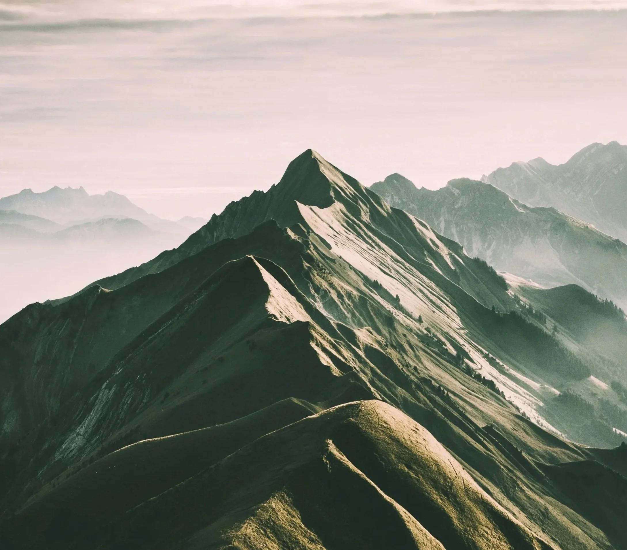 Bergkette mit mehreren Gipfeln, im Morgenlicht, mit Wolken im Hintergrund.