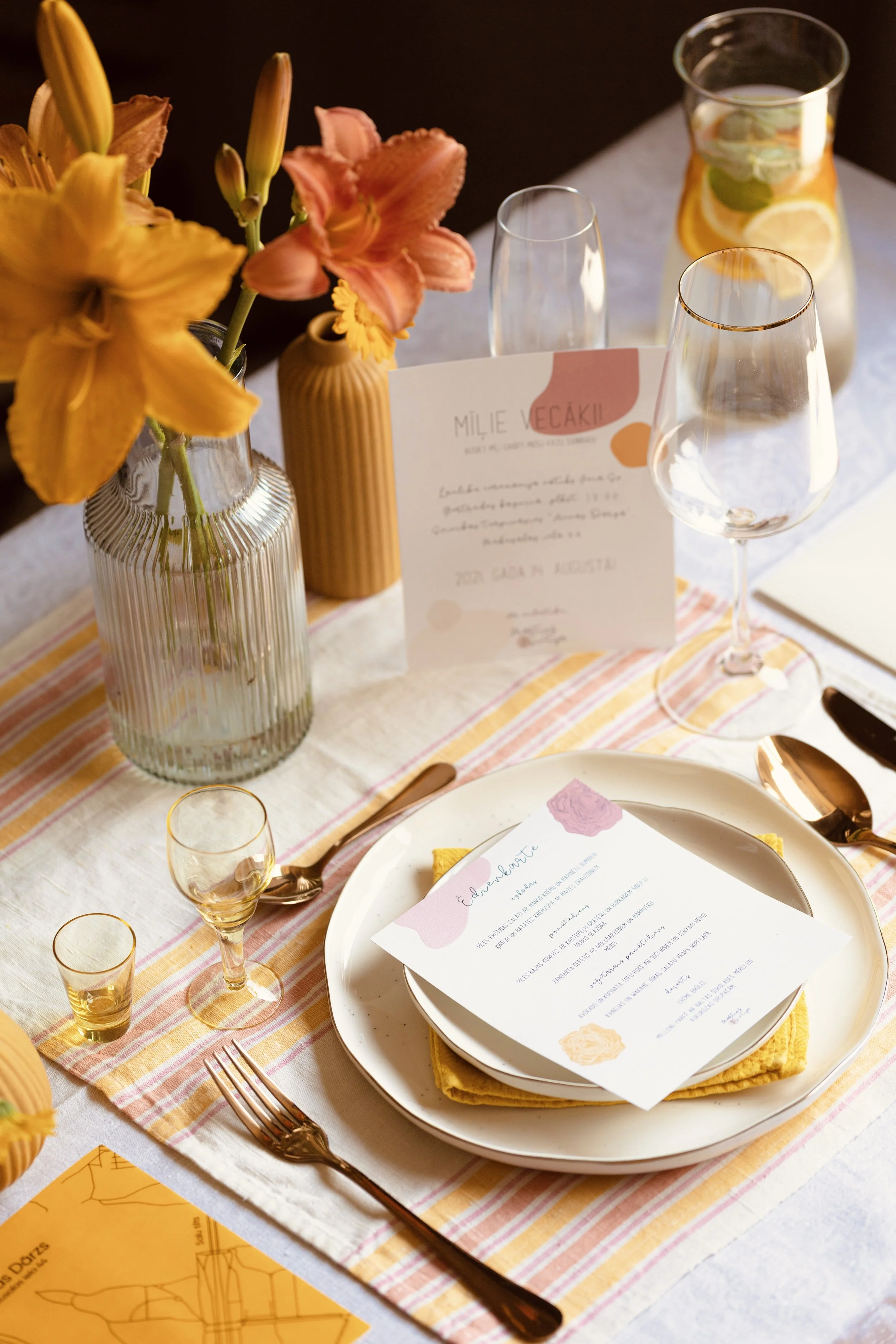 Table setting with floral centerpieces, empty wine glasses, a menu, and pink and orange decor for a celebration or event.