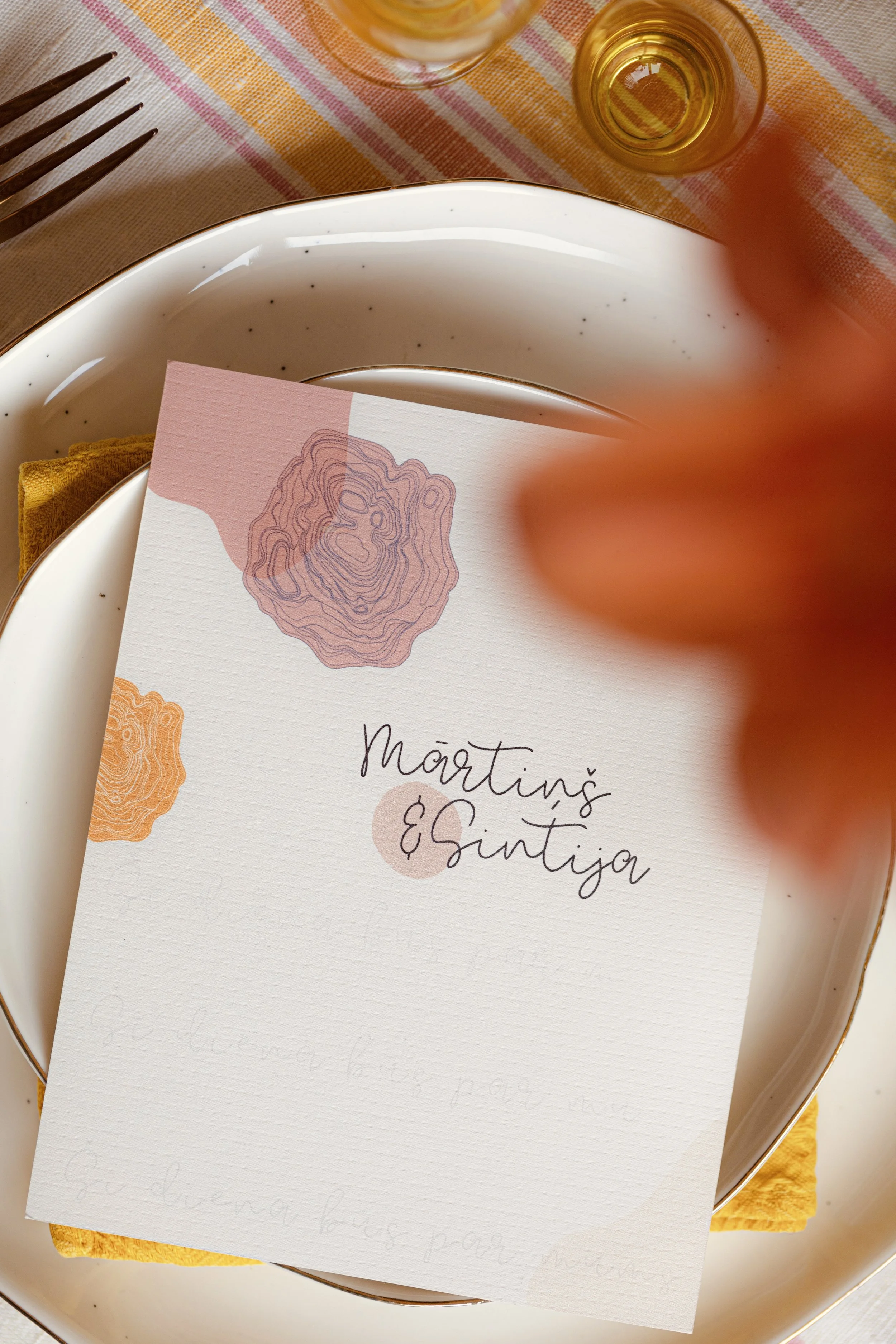 Wedding invitation for Martin and Sintja on a white plate with a yellow napkin, set on a striped tablecloth, with a glass of beer and a glass of light-colored beverage in the background.
