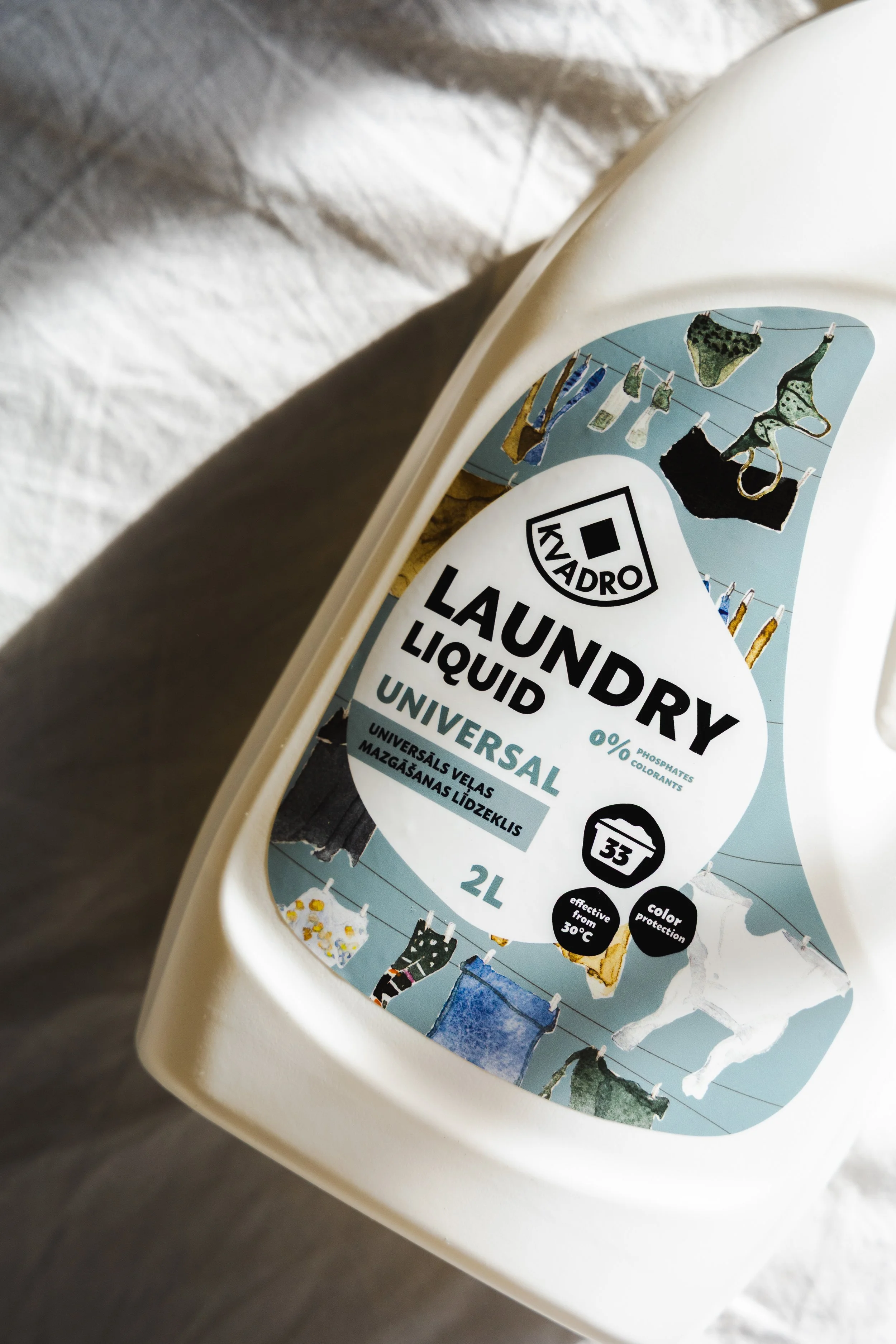 A bottle of laundry liquid with a white and blue label. The label features illustrations of laundry hung on clotheslines and includes text indicating it is universal, 2 liters, effective from 30°C, and color protection.