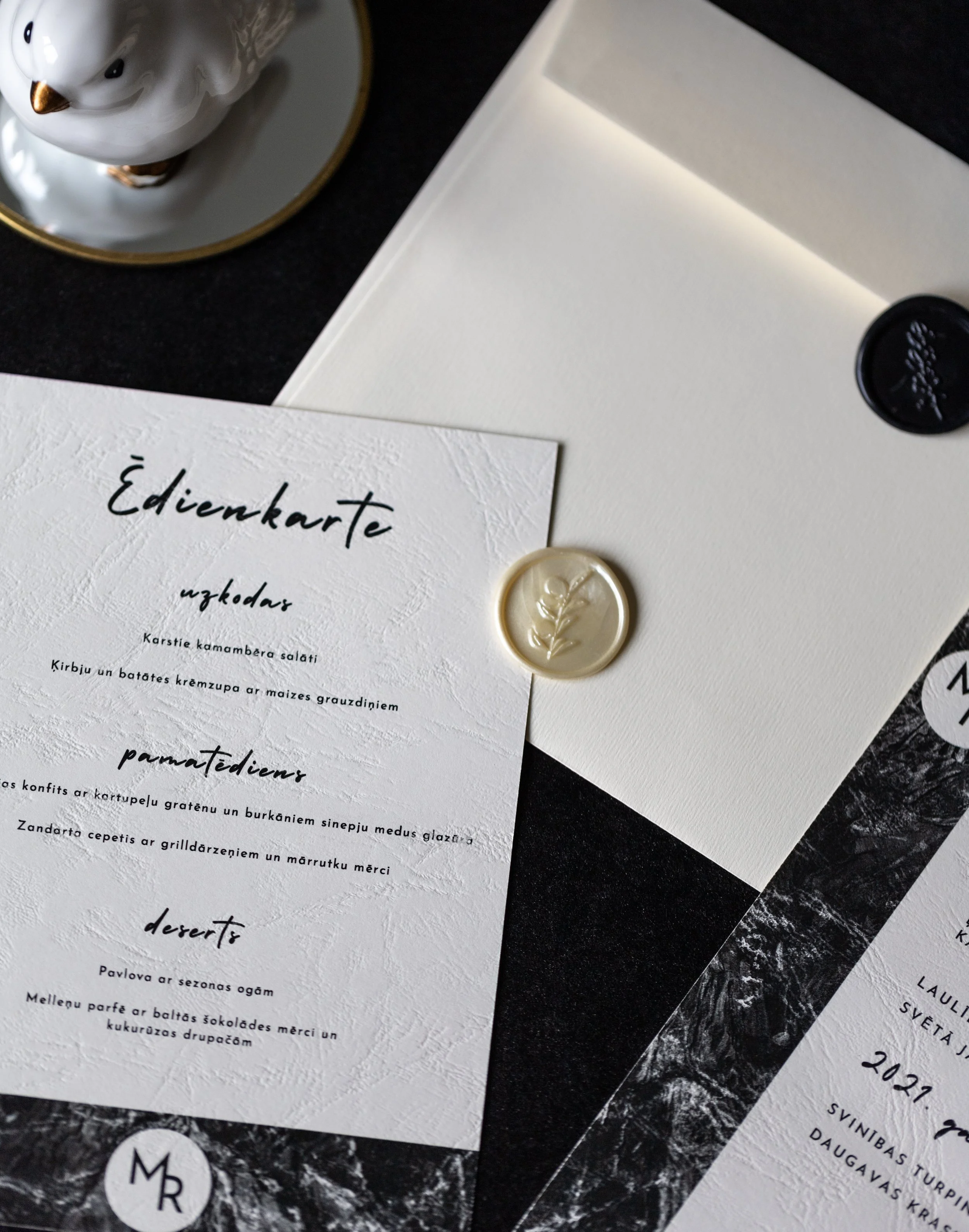 Wedding invitation card with textured white paper, black calligraphy, gold wax seal, and partially visible details.