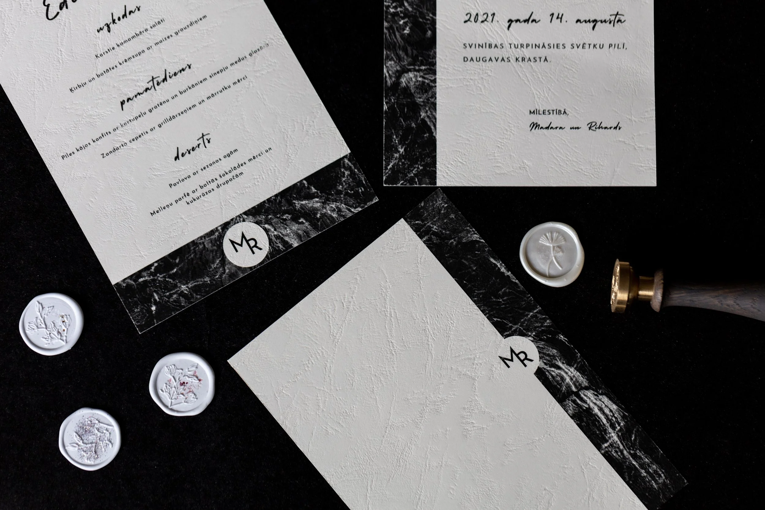 Wedding invitations and wax seals with botanical and marble design, written in Latvian, on a black background.