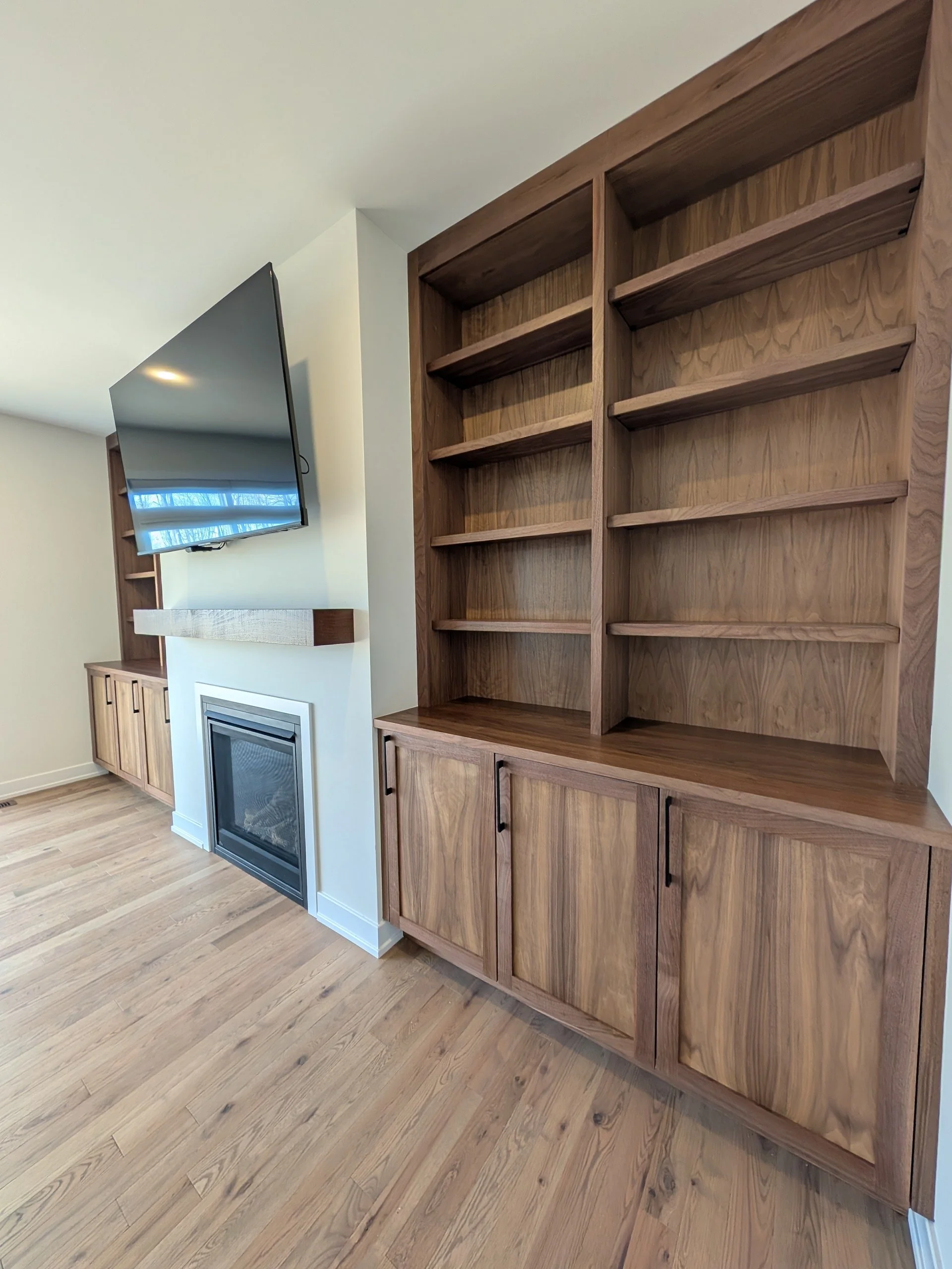 Empty wooden bookshelf in living room with built-in cabinets below and a TV mounted on the wall.