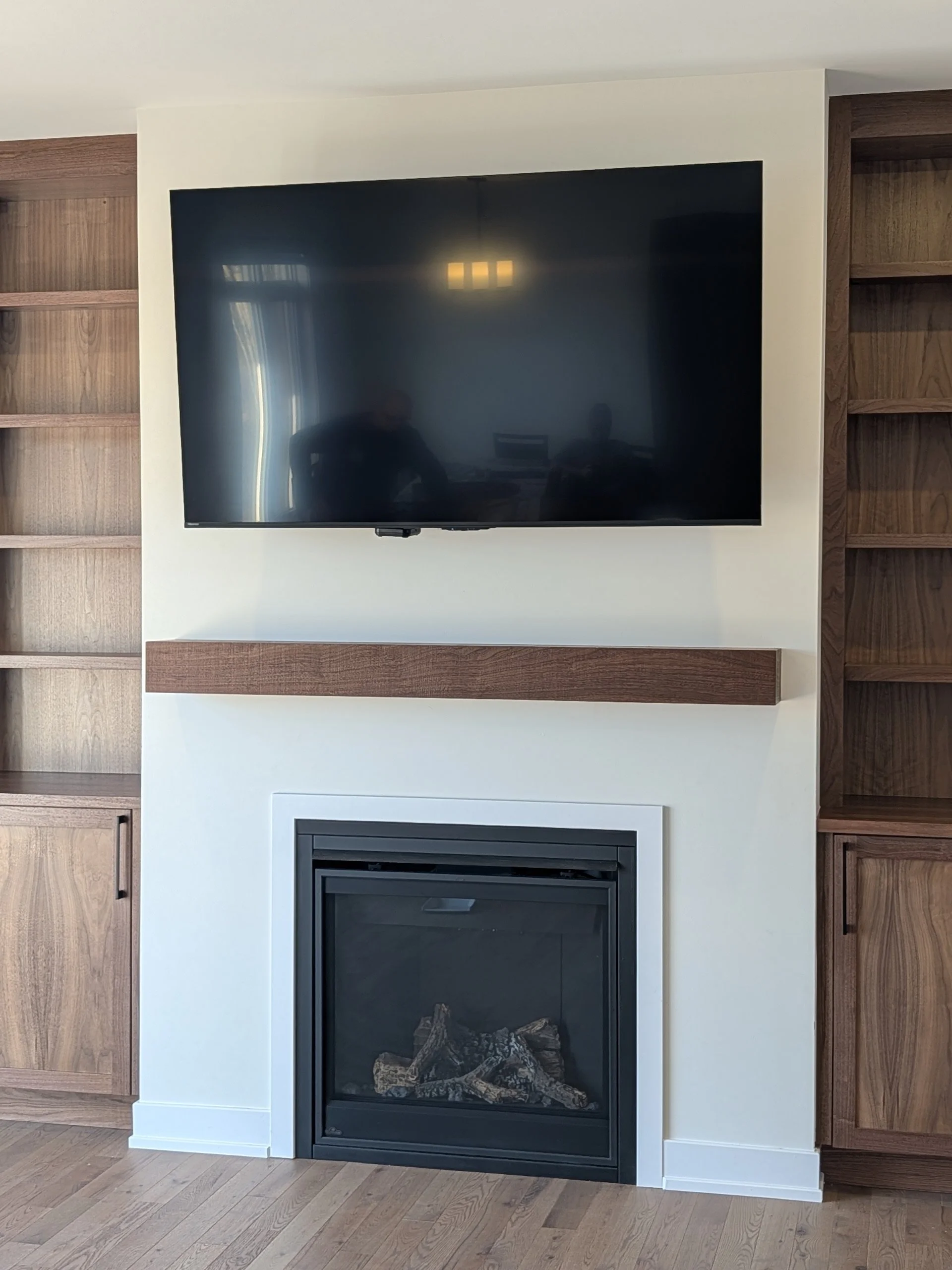 Living room with a wall-mounted flat-screen TV above a fireplace with logs, flanked by wooden bookshelves.