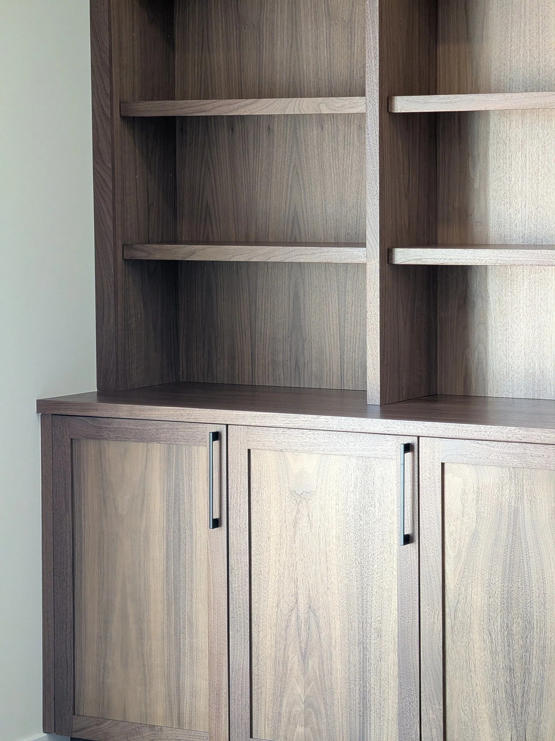 A wooden cabinet with open shelves on top and closed doors below, featuring black handles.