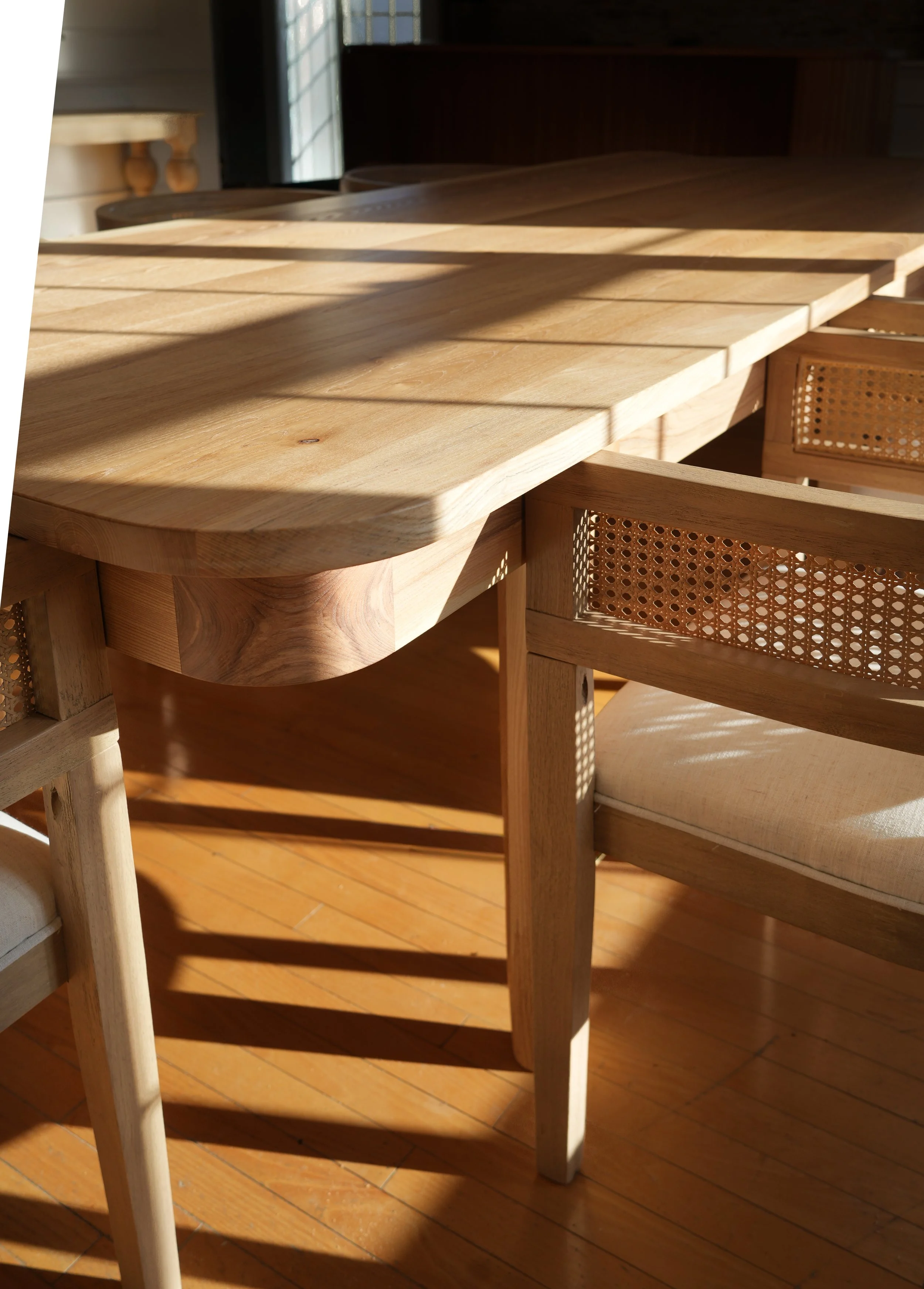 Wooden dining table with chairs, sunlight casting shadows on the floor.