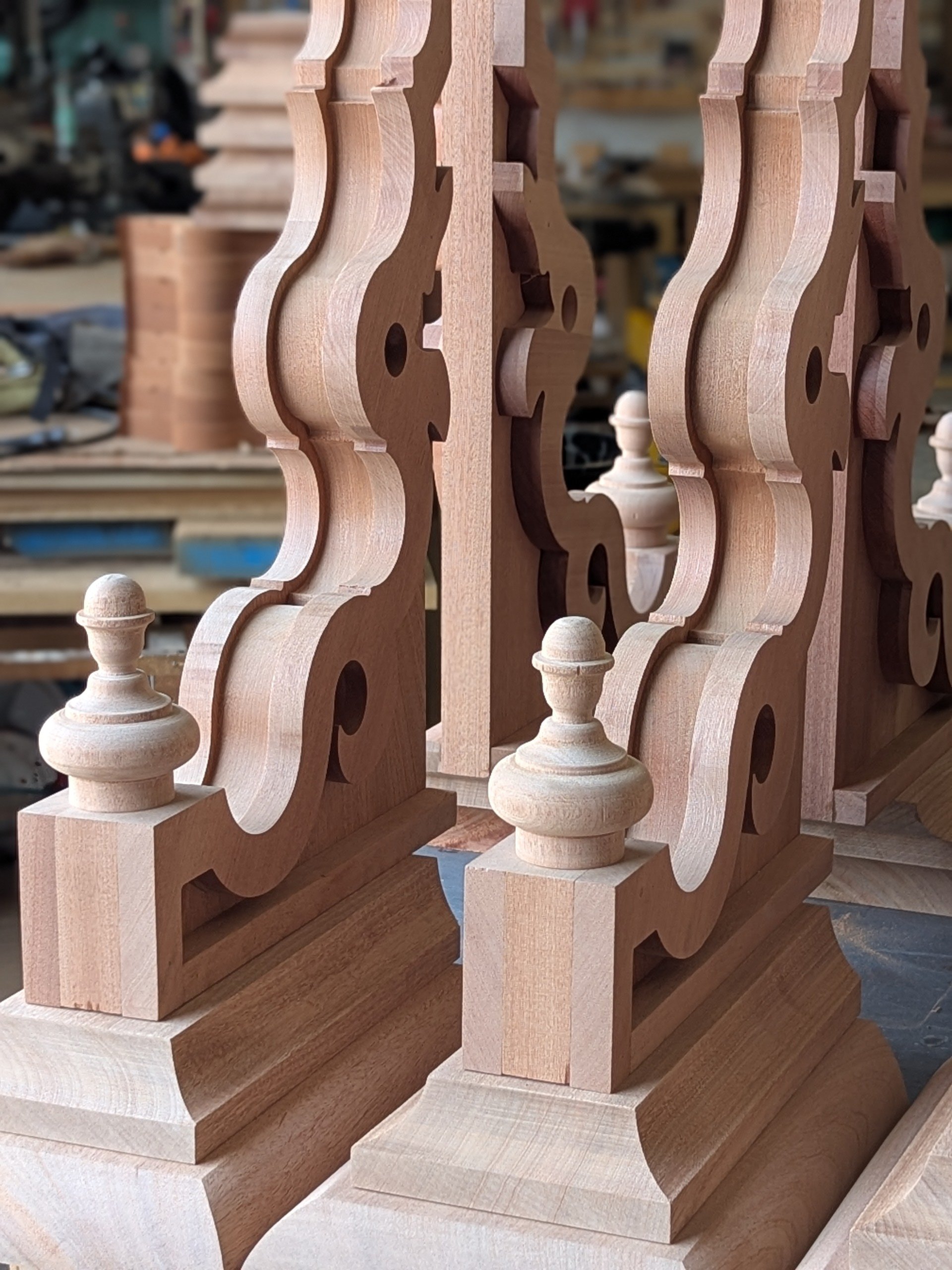 Close-up of unfinished wooden balustrades with intricate carved details in a woodworking shop.