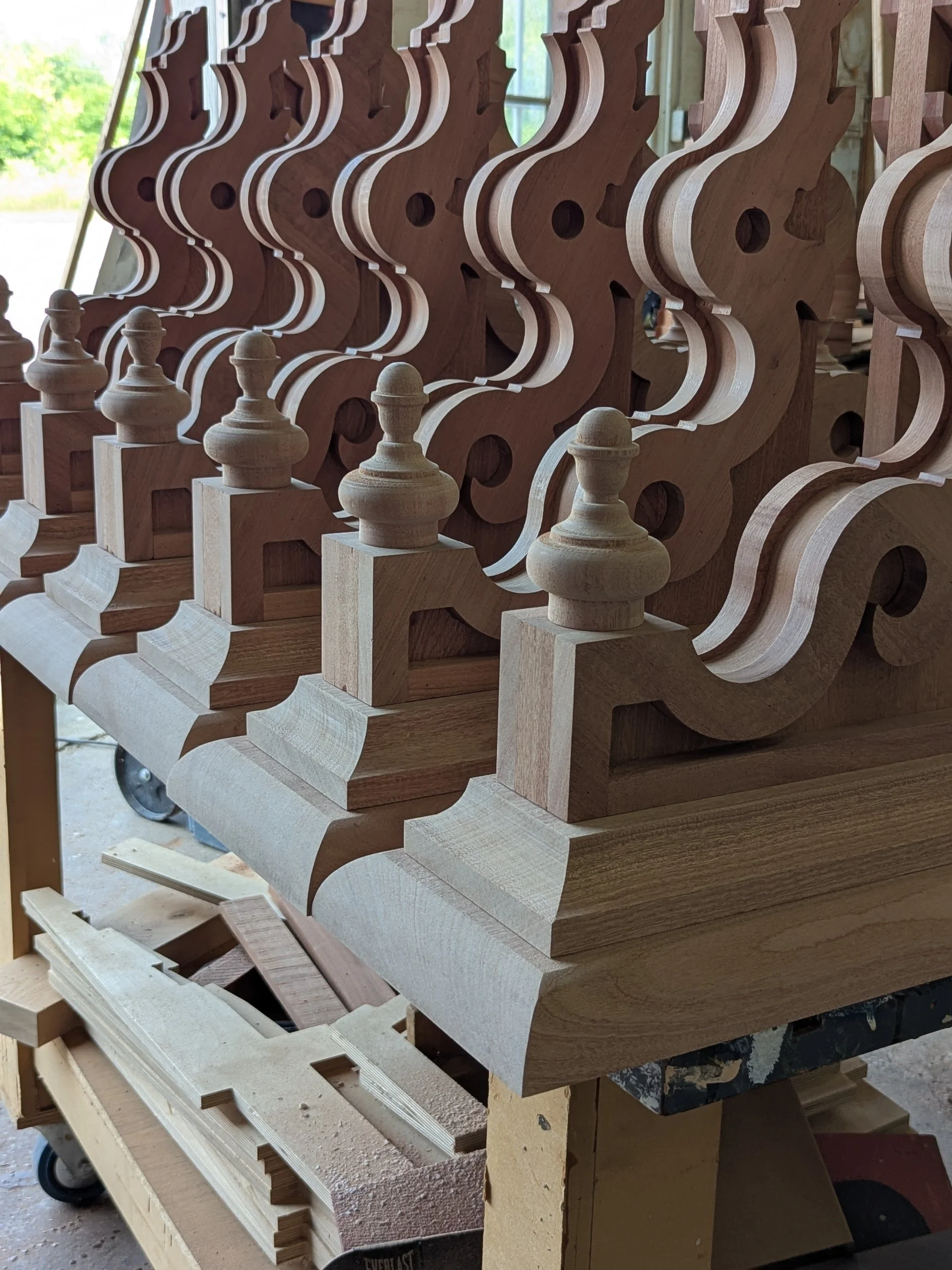 Multiple wooden chess pieces and chessboard parts in a woodworking shop.