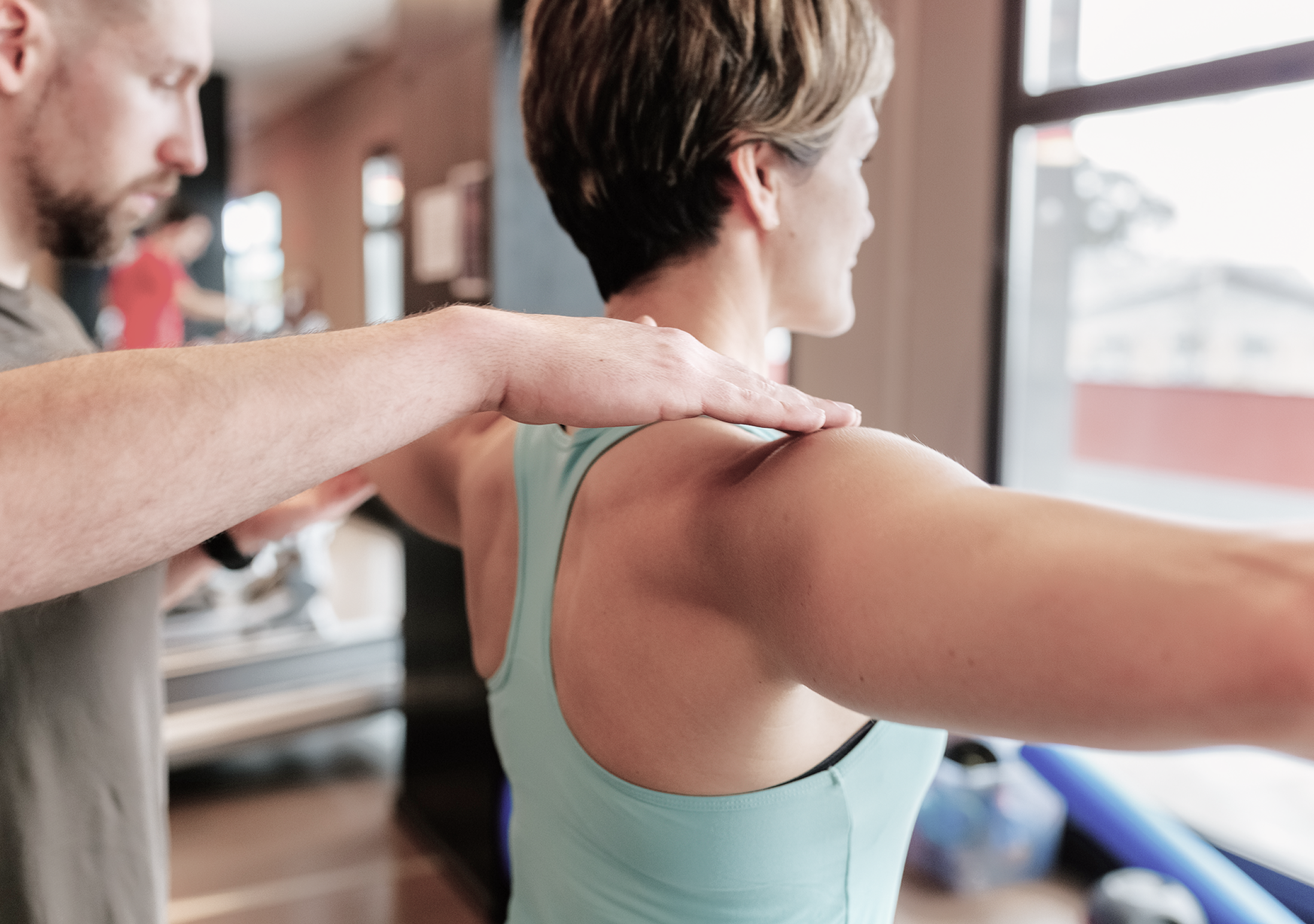 A professional providing hands-on guidance as a person holds their arms outstretched during a movement exercise.