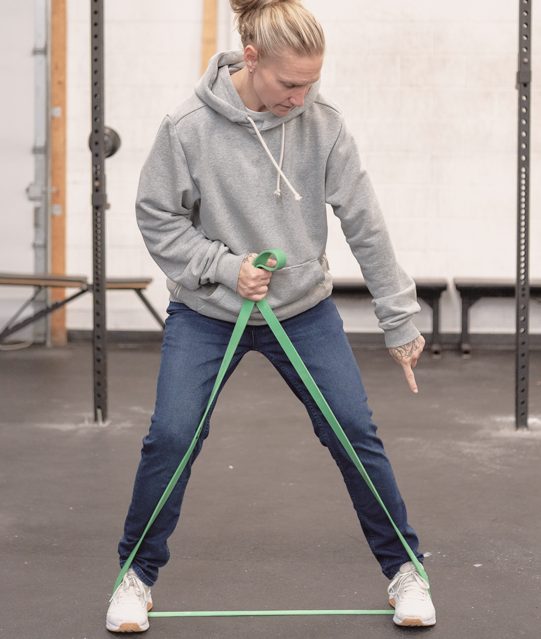 A professional demonstrating a resistance band exercise while pointing to proper foot placement.