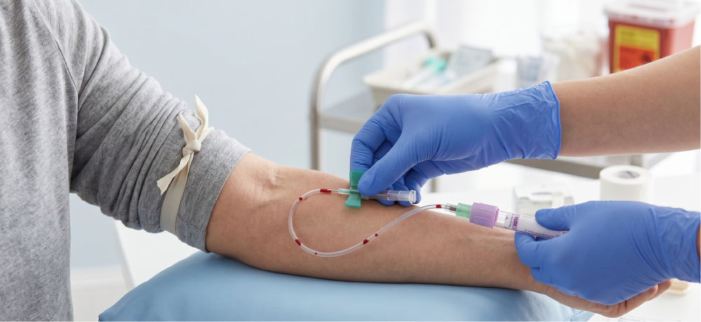 A healthcare professional wearing blue gloves is inserting a needle into a patient's arm for blood draw in a clinical setting.