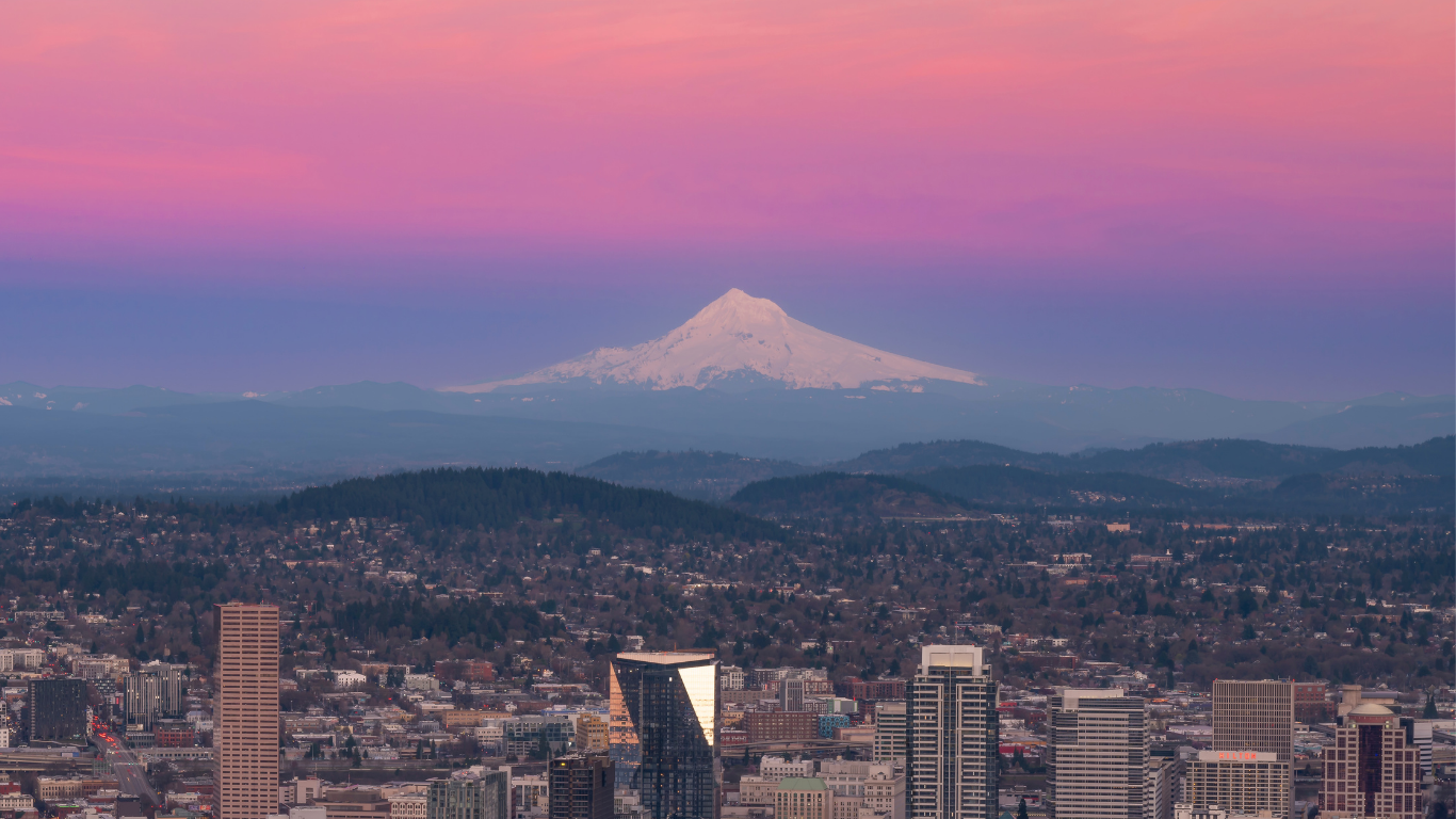 Skyline of Portland, Oregon with snow-capped Mount Hood in the background during sunset, pink and purple sky over city skyscrapers and hills by Parker Penley