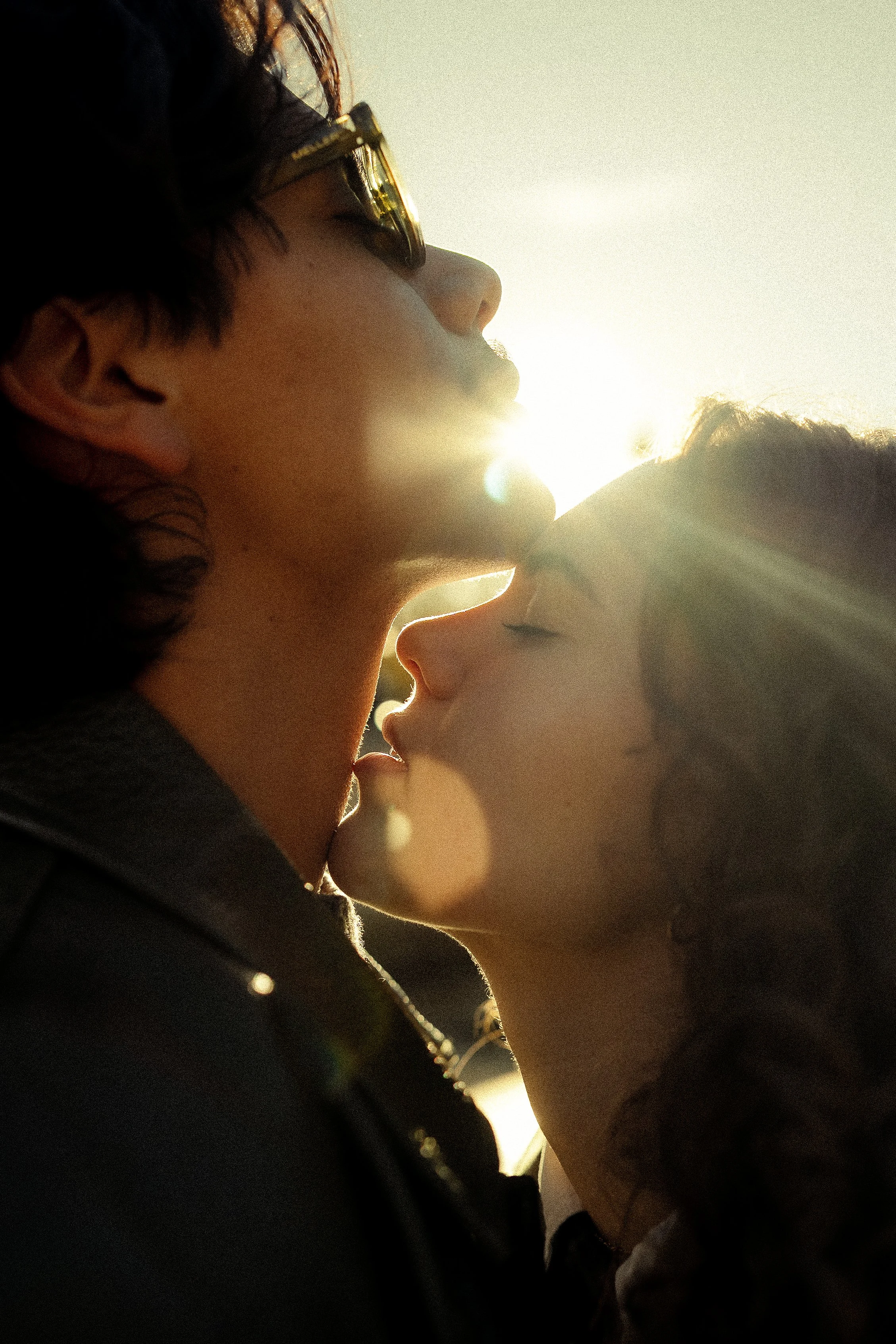 A couple kissing with the sun shining behind them, creating a warm glow and lens flare.