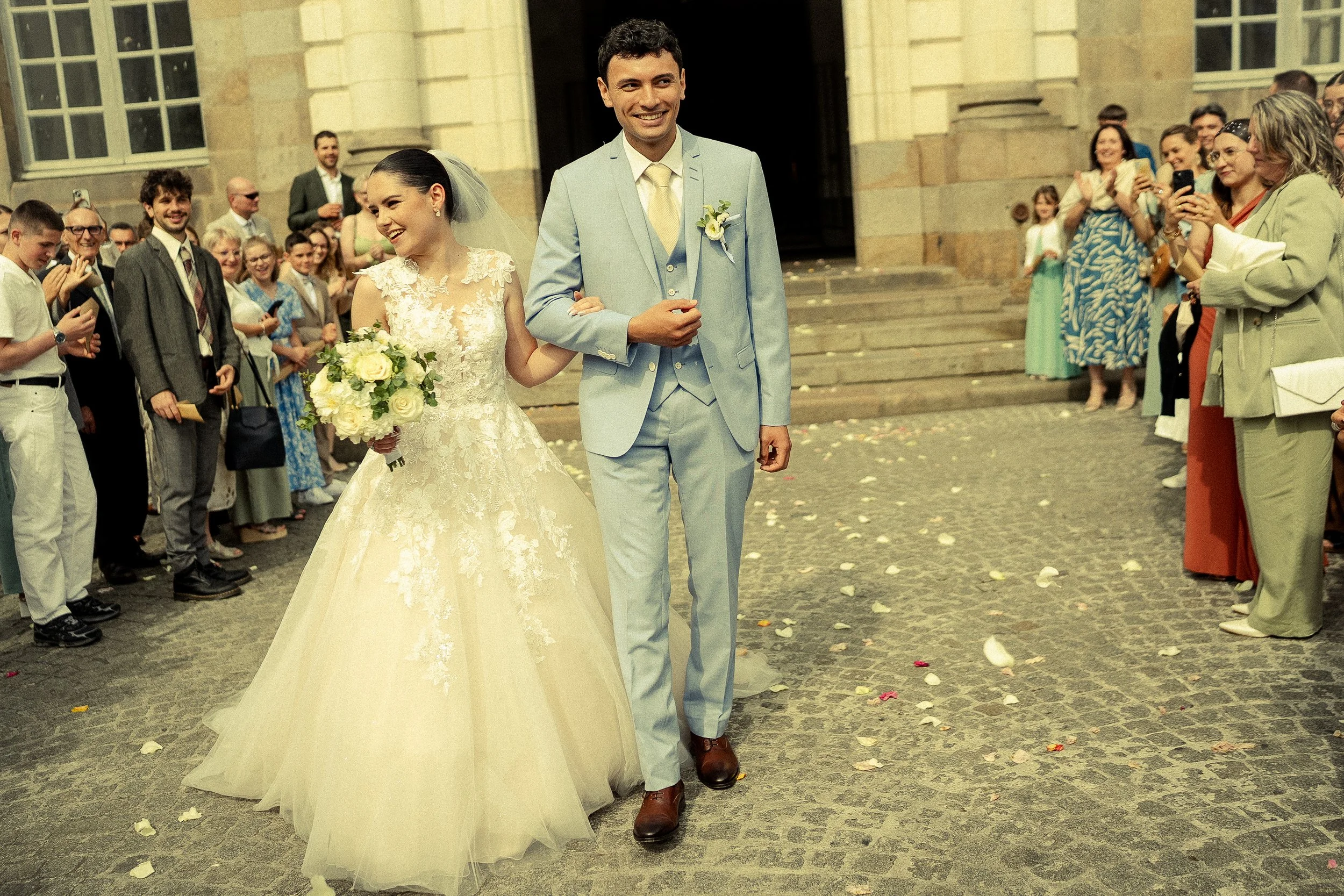 Un couple de mariés sortant de l'église, entouré de invités heureux qui prennent des photos.