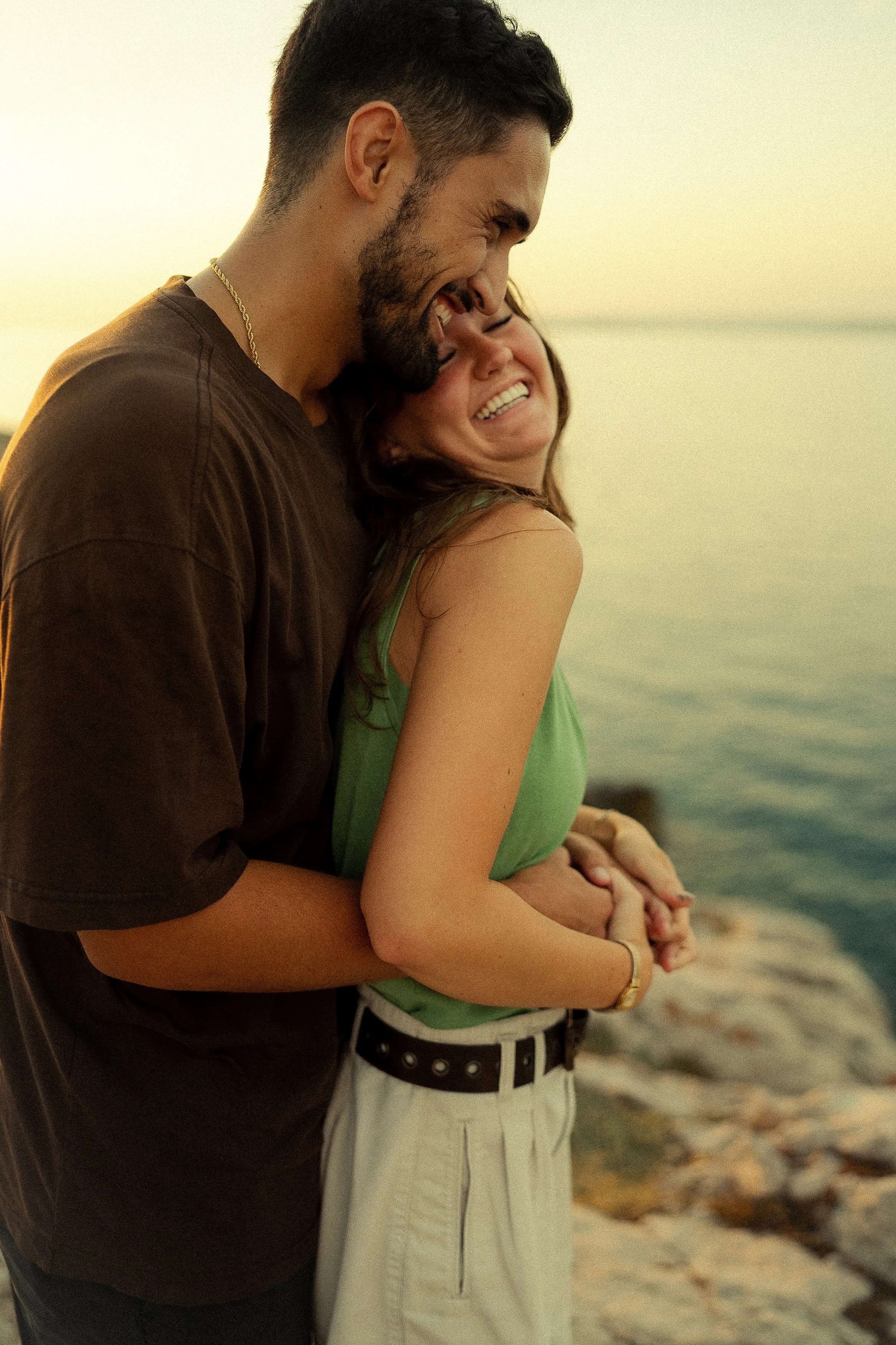 un couple qui rigole ensemble devant la mer et le couché de soleil