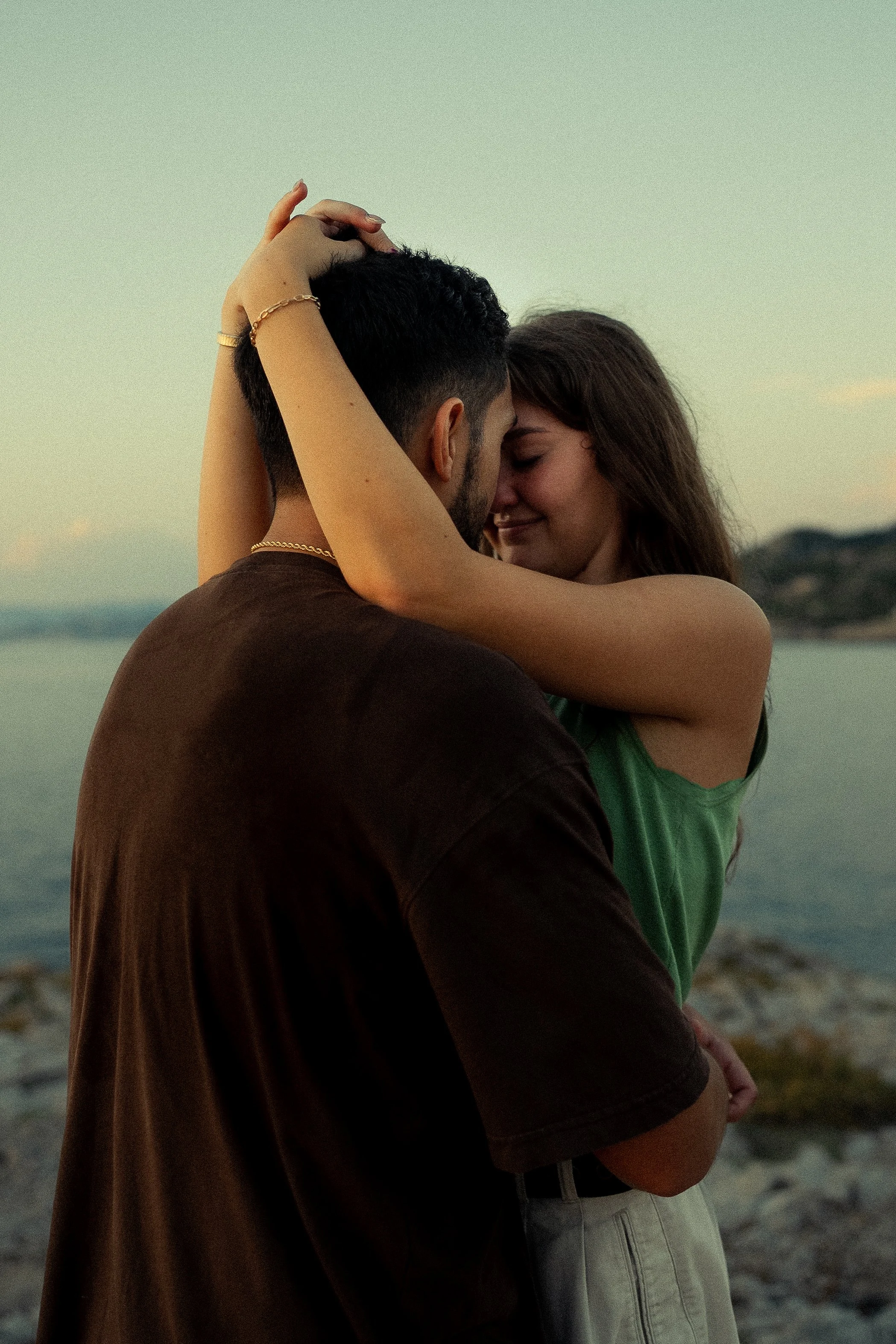 Un couple enlaçant leur front, souriant avec tendresse, à la plage au coucher du soleil.