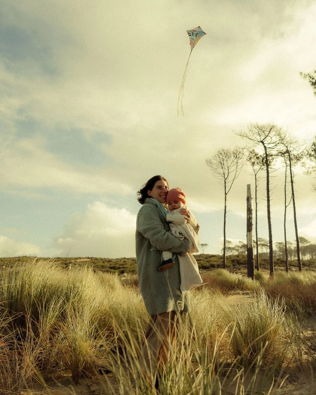 une maman avec son bébé dans les bras et un cerf volant qui vole au dessus de sa tête