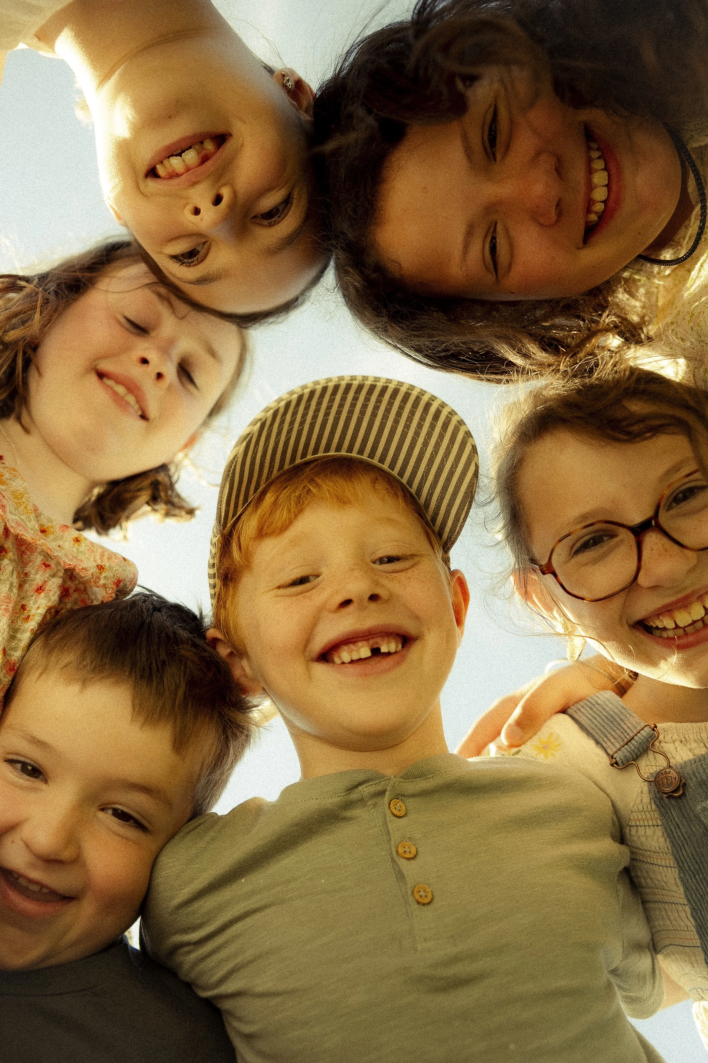 Un groupe d'enfants souriants et riants, pris en photo durant une séance photo de famille par dessous avec le ciel en arrière-plan.