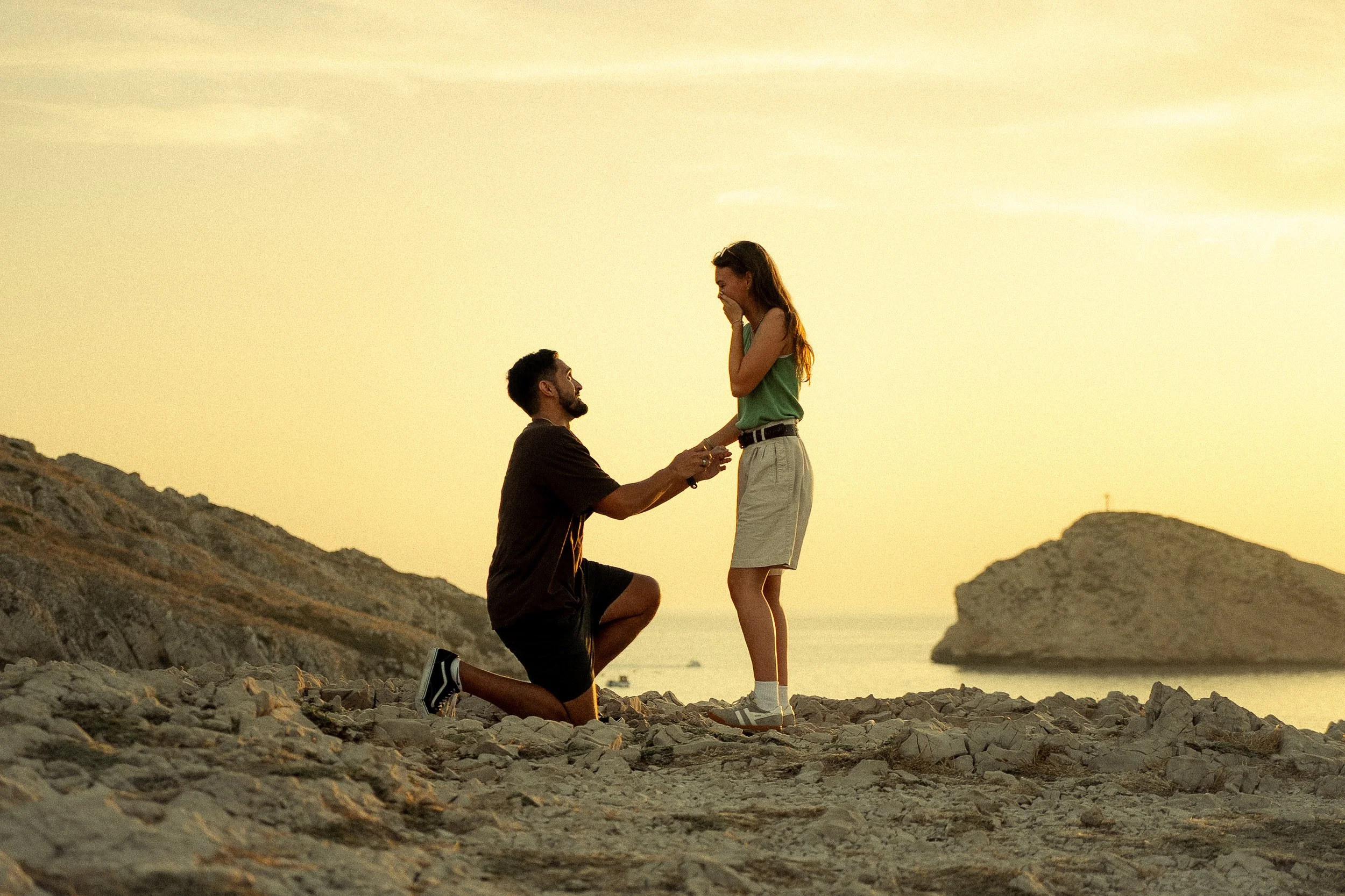 Un homme fait une proposition de mariage à une femme sur une plage au coucher du soleil.