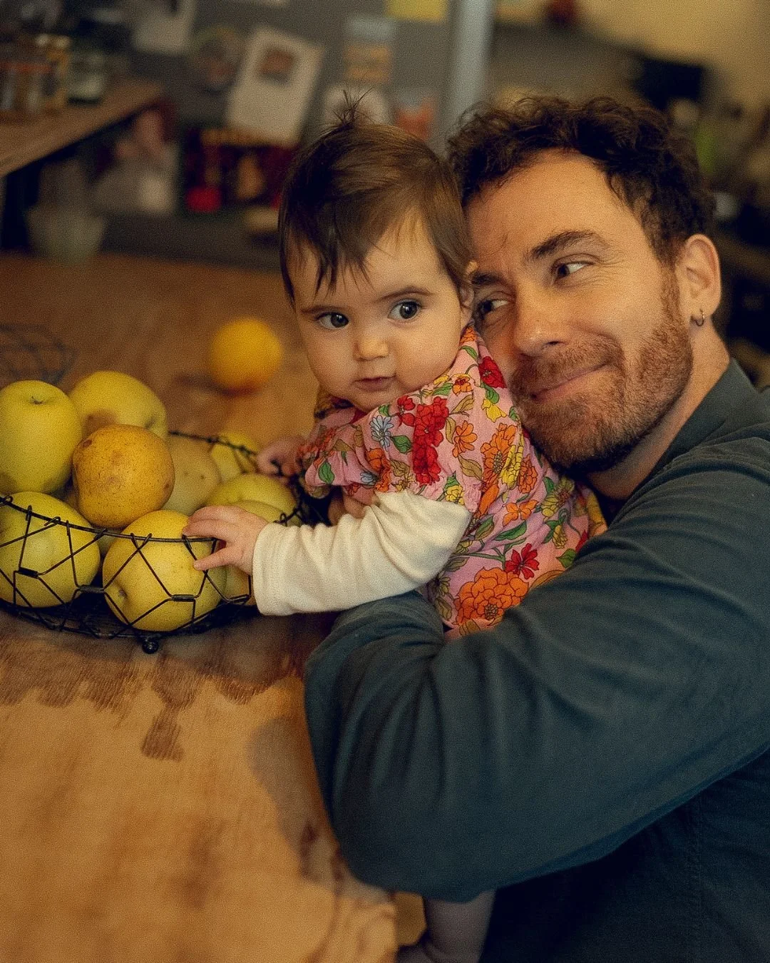 un papa qui a son bébé dans les bras devant un sac de pomme